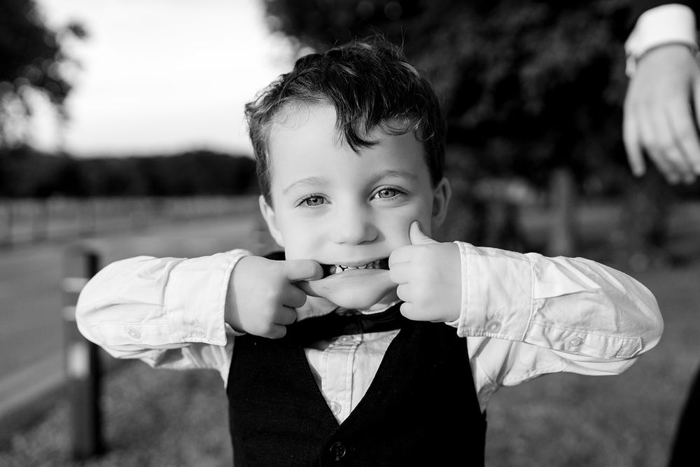 Black and white portrait of playful child wearing a vest and white shirt pulling a silly face.