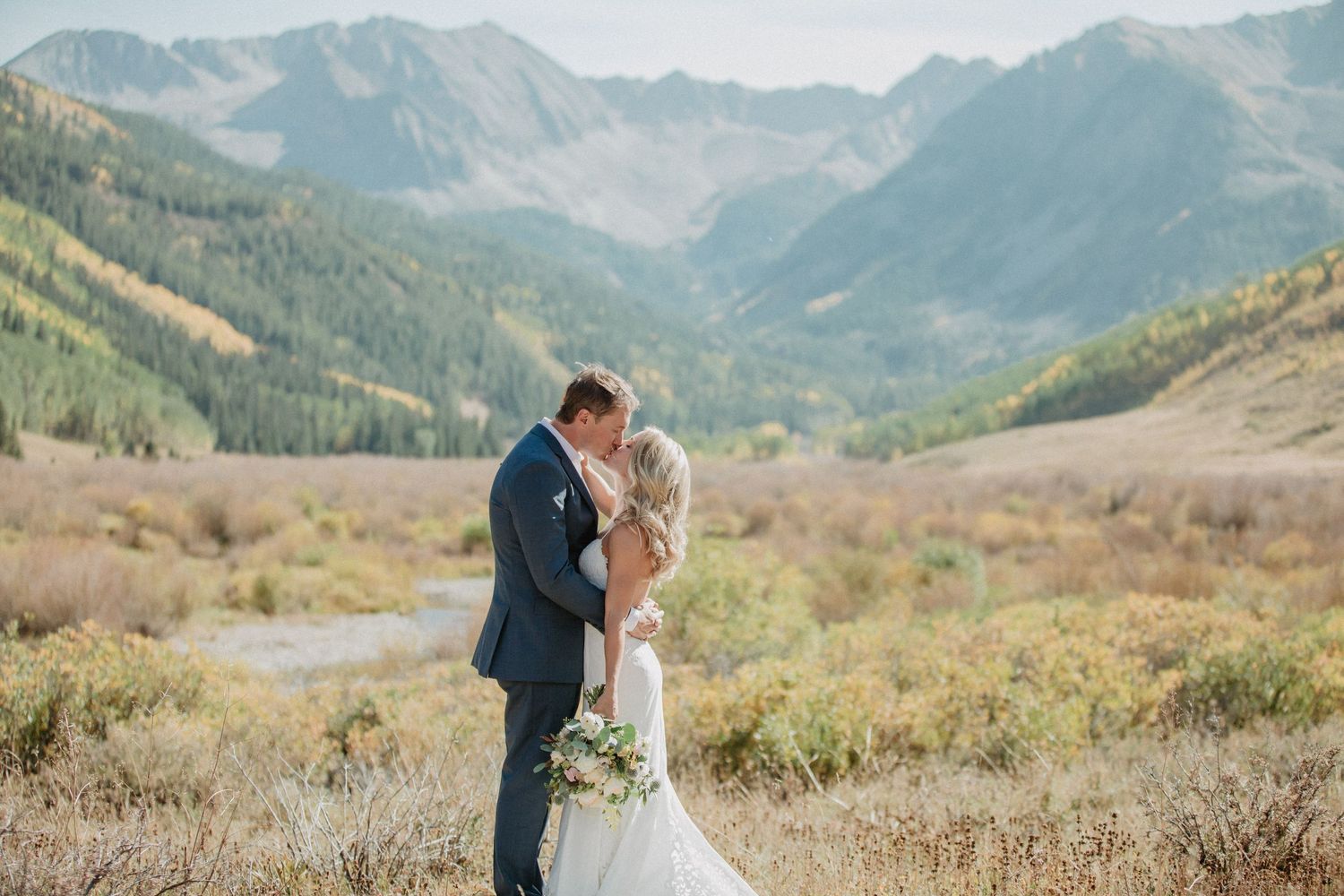 A couple in wedding attire embrace against a backdrop of majestic mountains in Aspen. Elopement photos at sunset.