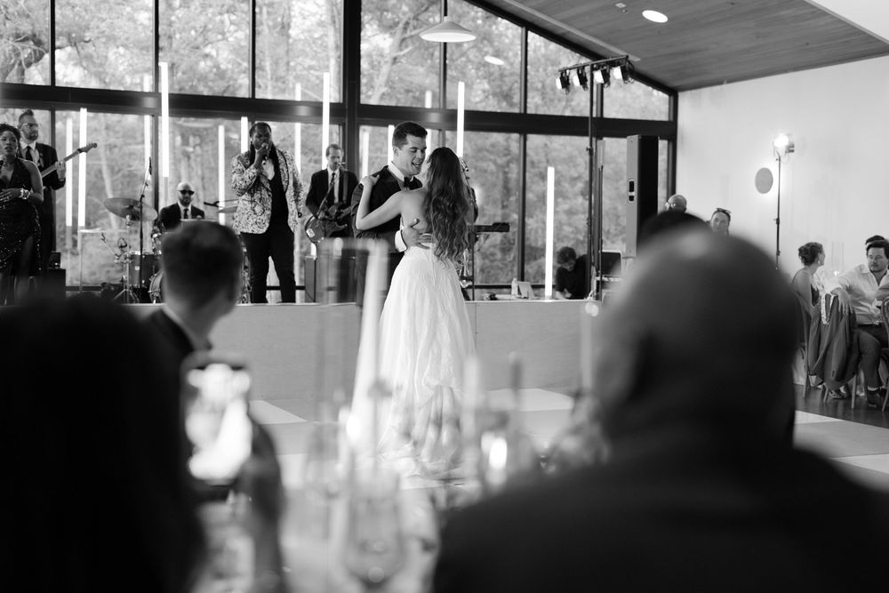Black and white photo of a wedding reception with guests seated at tables while dancing occurs on the dance floor.