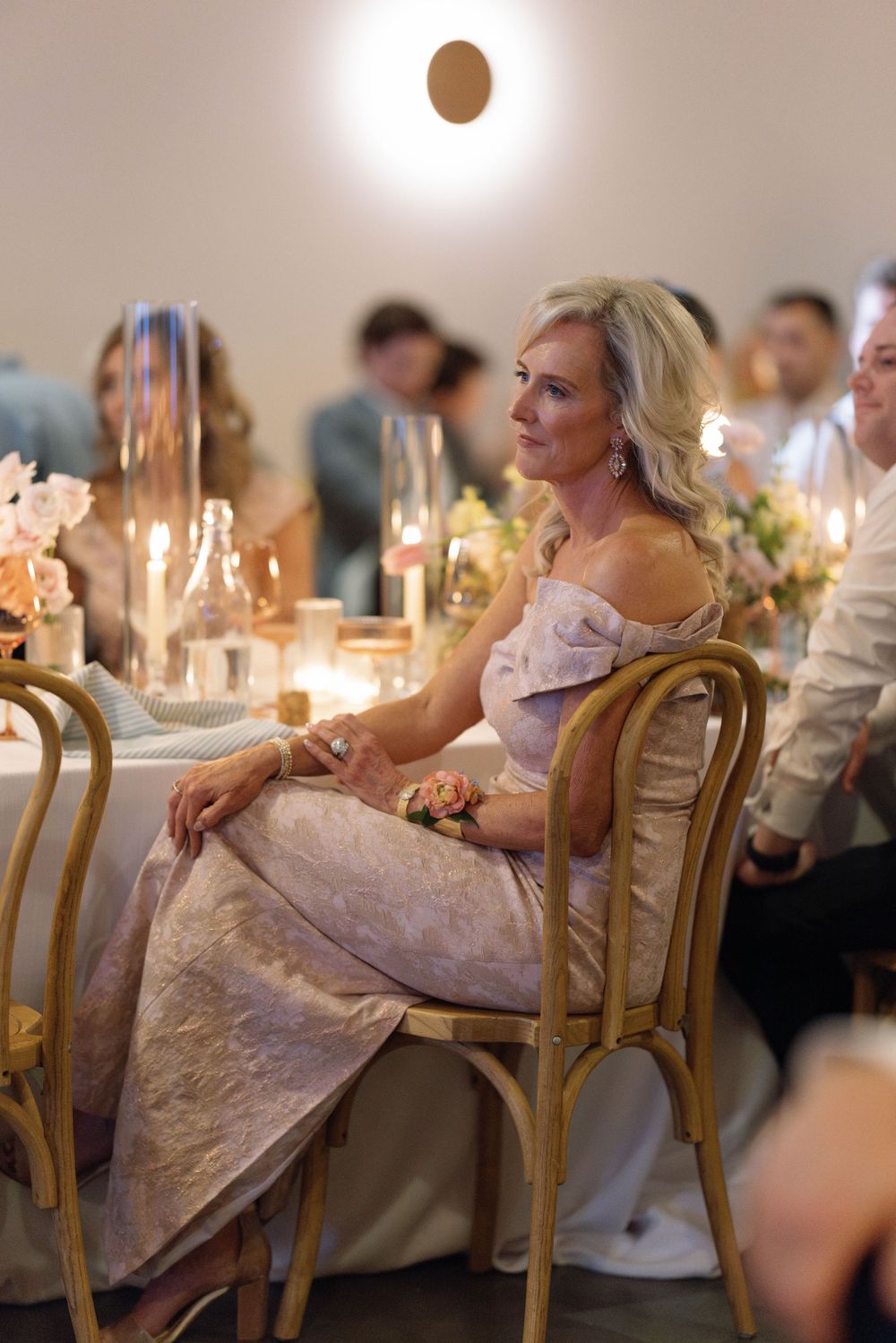 A guest in an elegant pink gown sits at a candlelit reception dinner at a formal event with gold chairs.