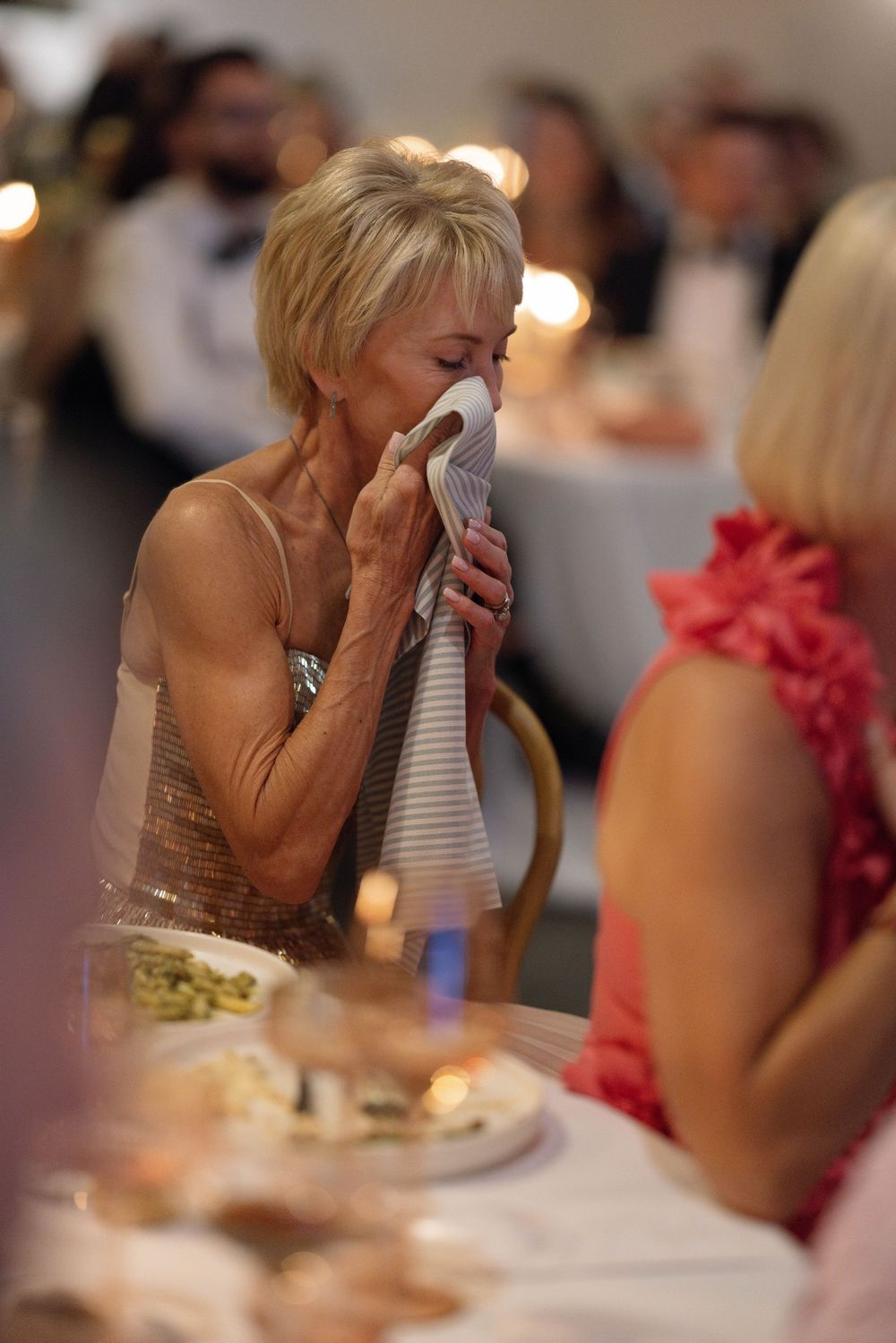 Two people are seen having an emotional moment at a formal table setting with soft lighting in the background.