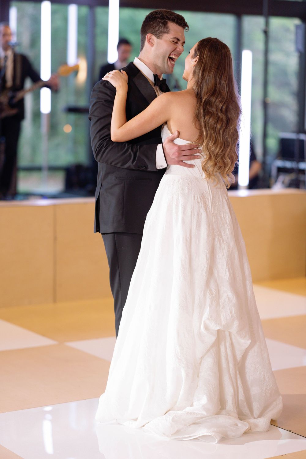 A couple shares their first dance at a wedding reception, with the bride in a flowing white gown and groom in dark suit.