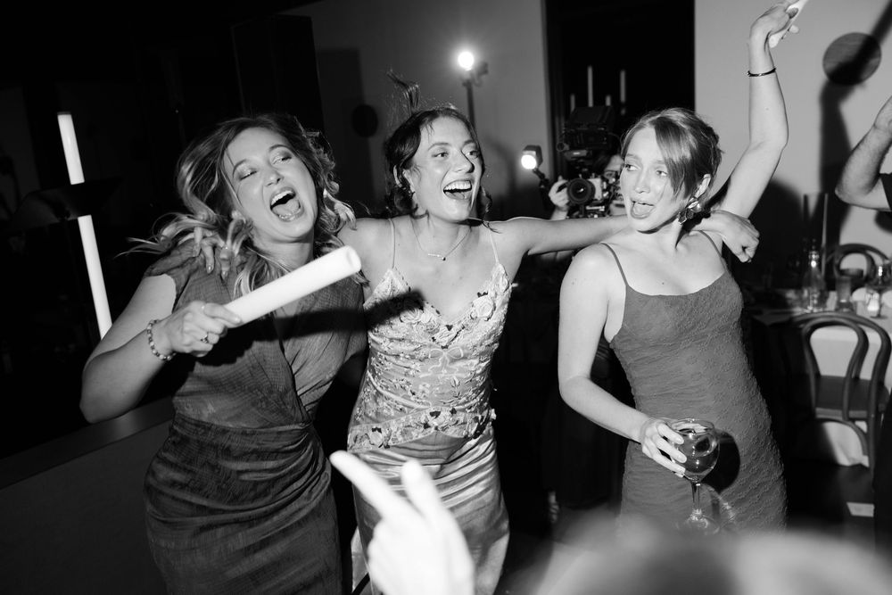 Three people dancing and laughing energetically together at what appears to be a party or celebration in black and white.