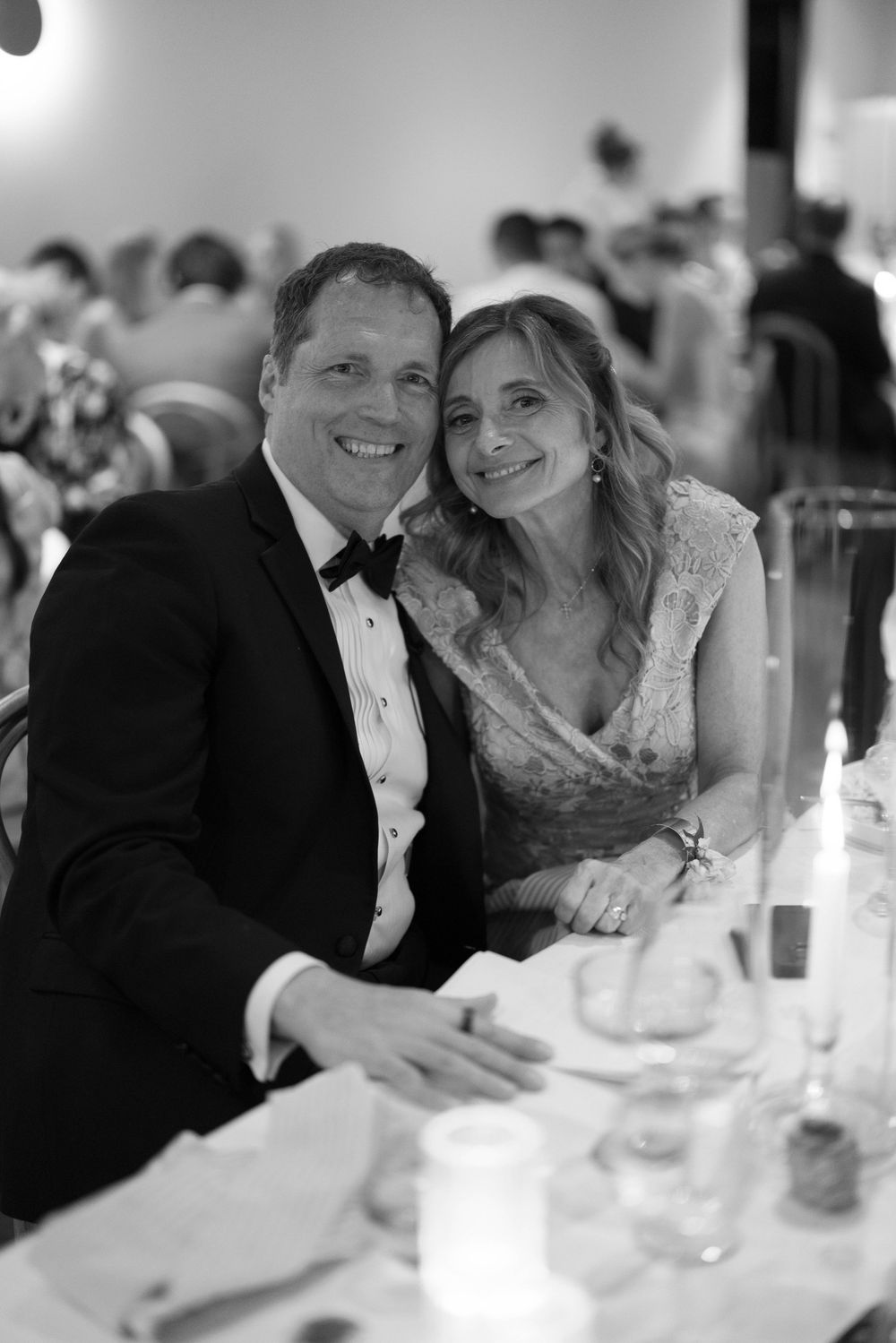 A couple in formal attire share an intimate moment at an elegant reception table in black and white photography.