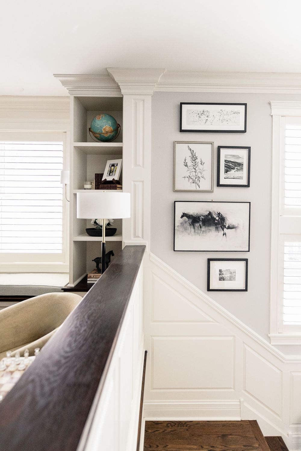 A stairway wall gallery features black and white framed art prints above white wainscoting with built-in shelving displaying decor.