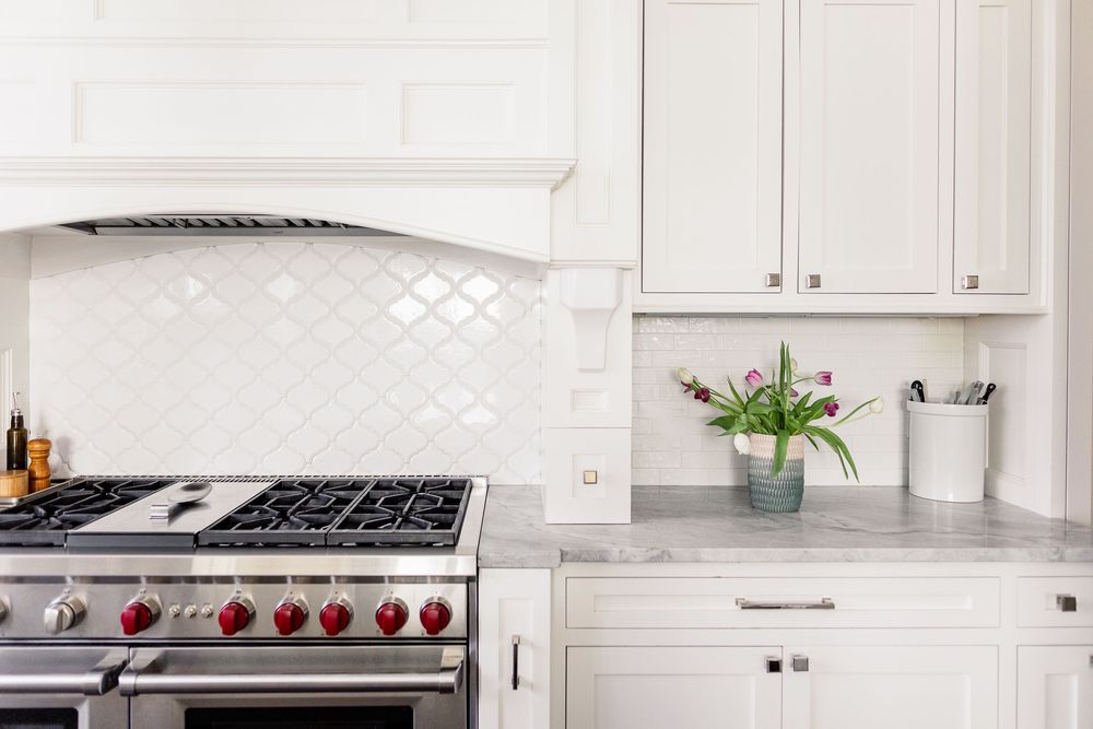 White kitchen with subway tile backsplash, stainless steel range, quartz countertops and white cabinets.