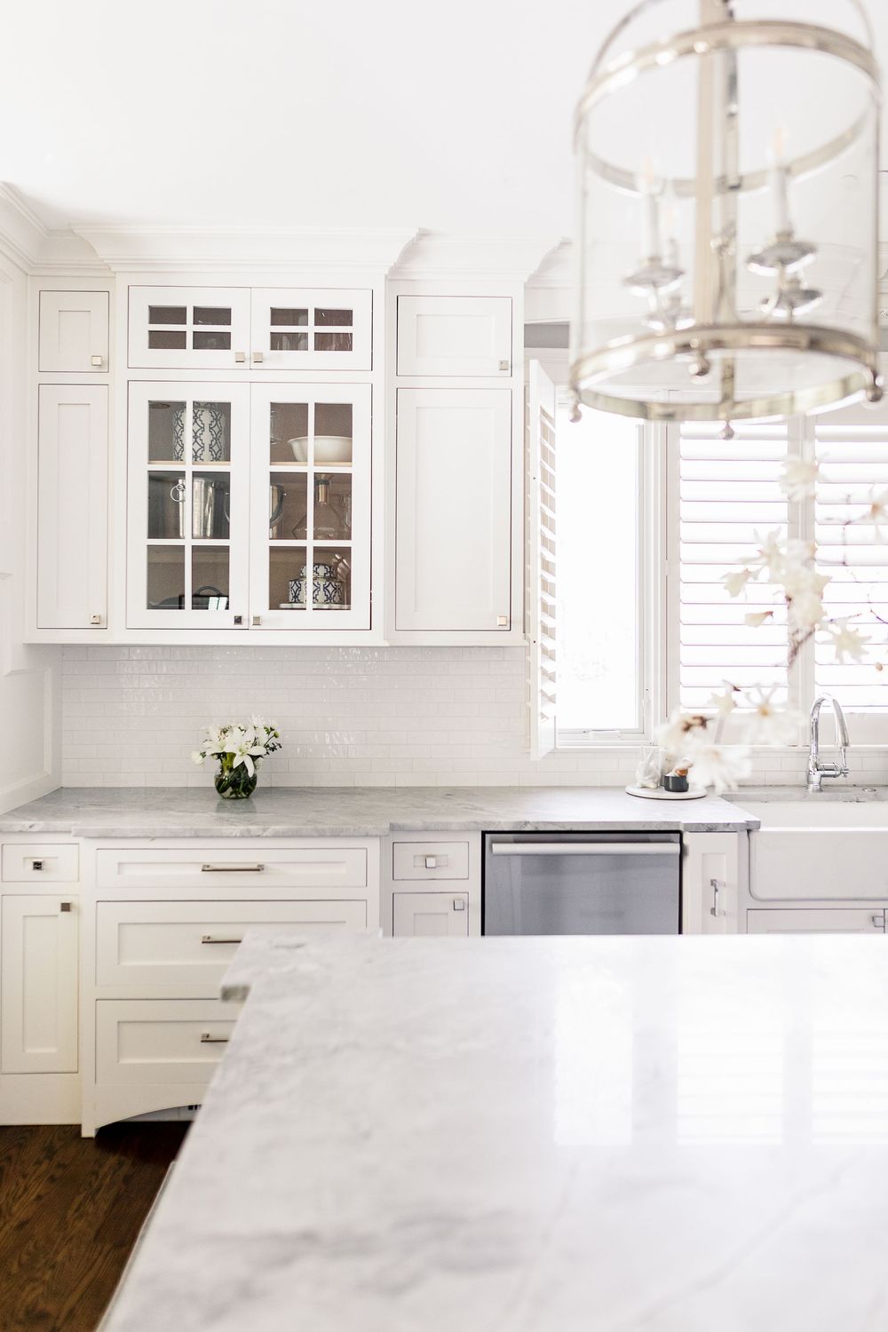Modern white kitchen with glass pendant lights, white cabinets, and marble countertops features a bright airy design.