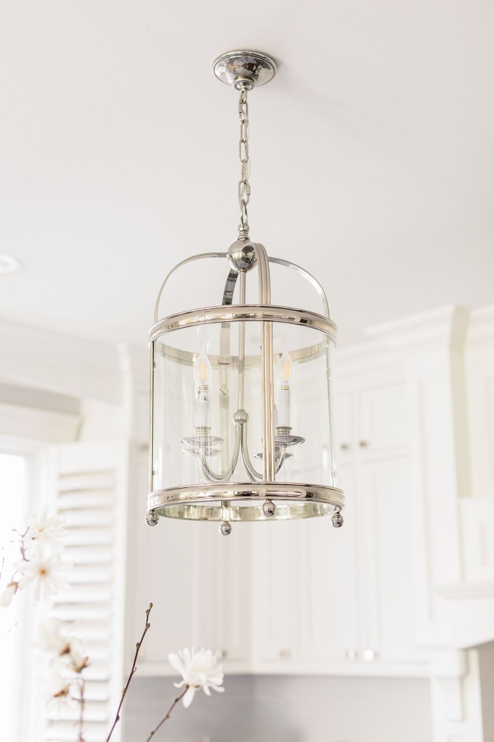 Elegant glass lantern pendant light with brushed nickel finish hangs from a chain in a bright white room.