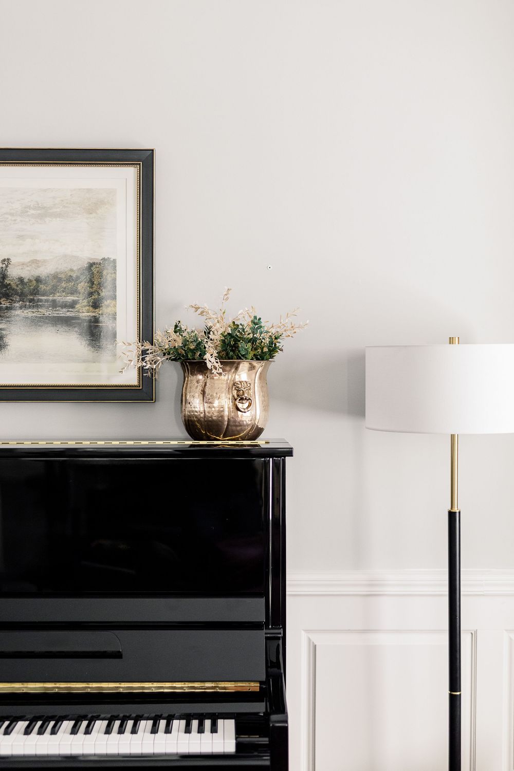 Elegant piano display with framed artwork and floral arrangement on a black upright piano against white walls.