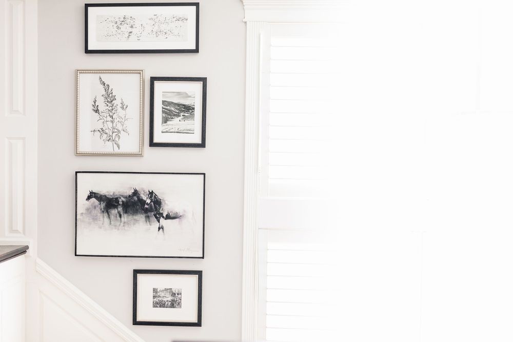 Gallery wall with black and white framed artwork including sketches and illustrations on a white painted wall.
