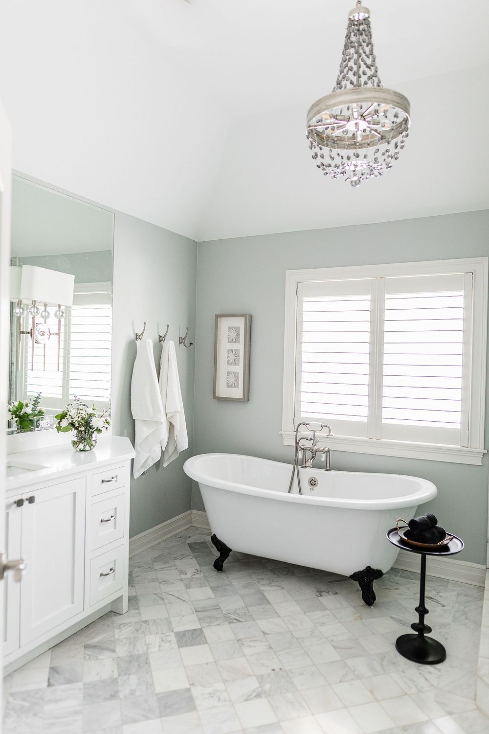 Luxurious white bathroom featuring clawfoot tub, crystal chandelier, and marble tile floors.