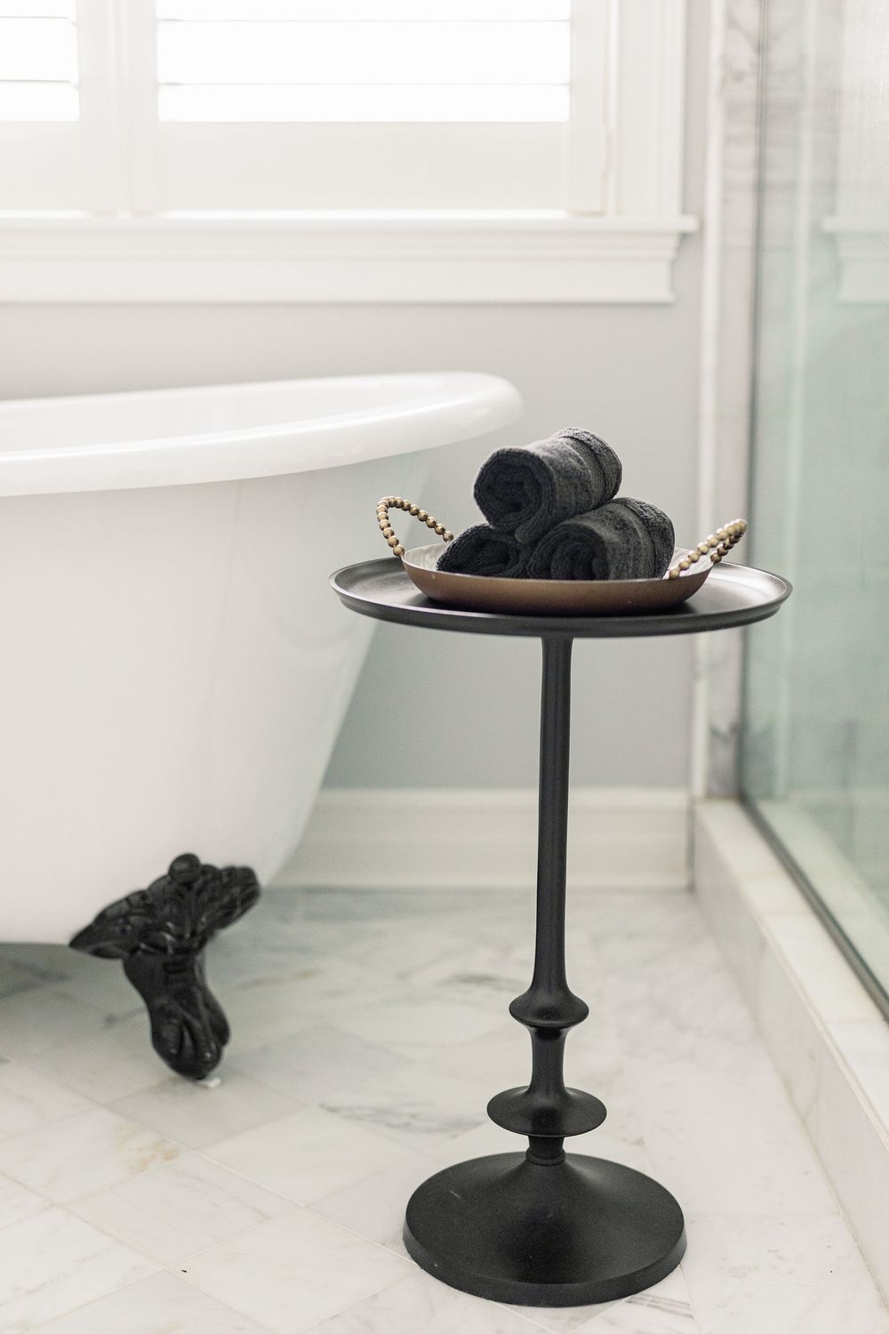 Black ceramic cake stand with decorative base displayed against white marble in minimalist bathroom setting.