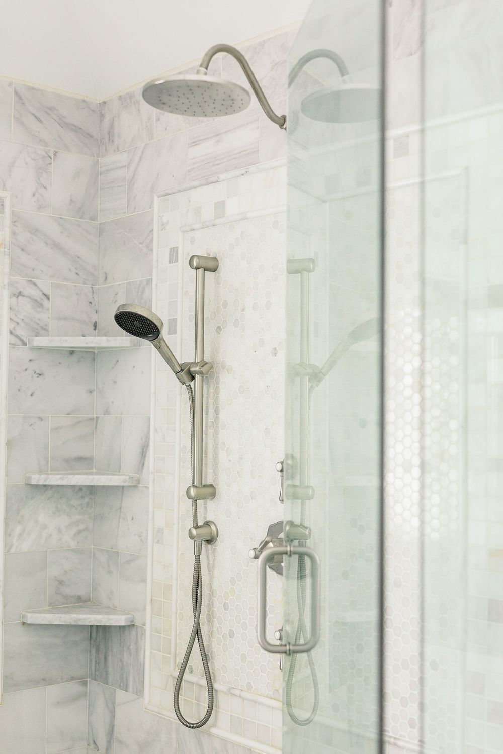 Modern marble bathroom with glass shower enclosure featuring brushed nickel fixtures and built-in shelving.