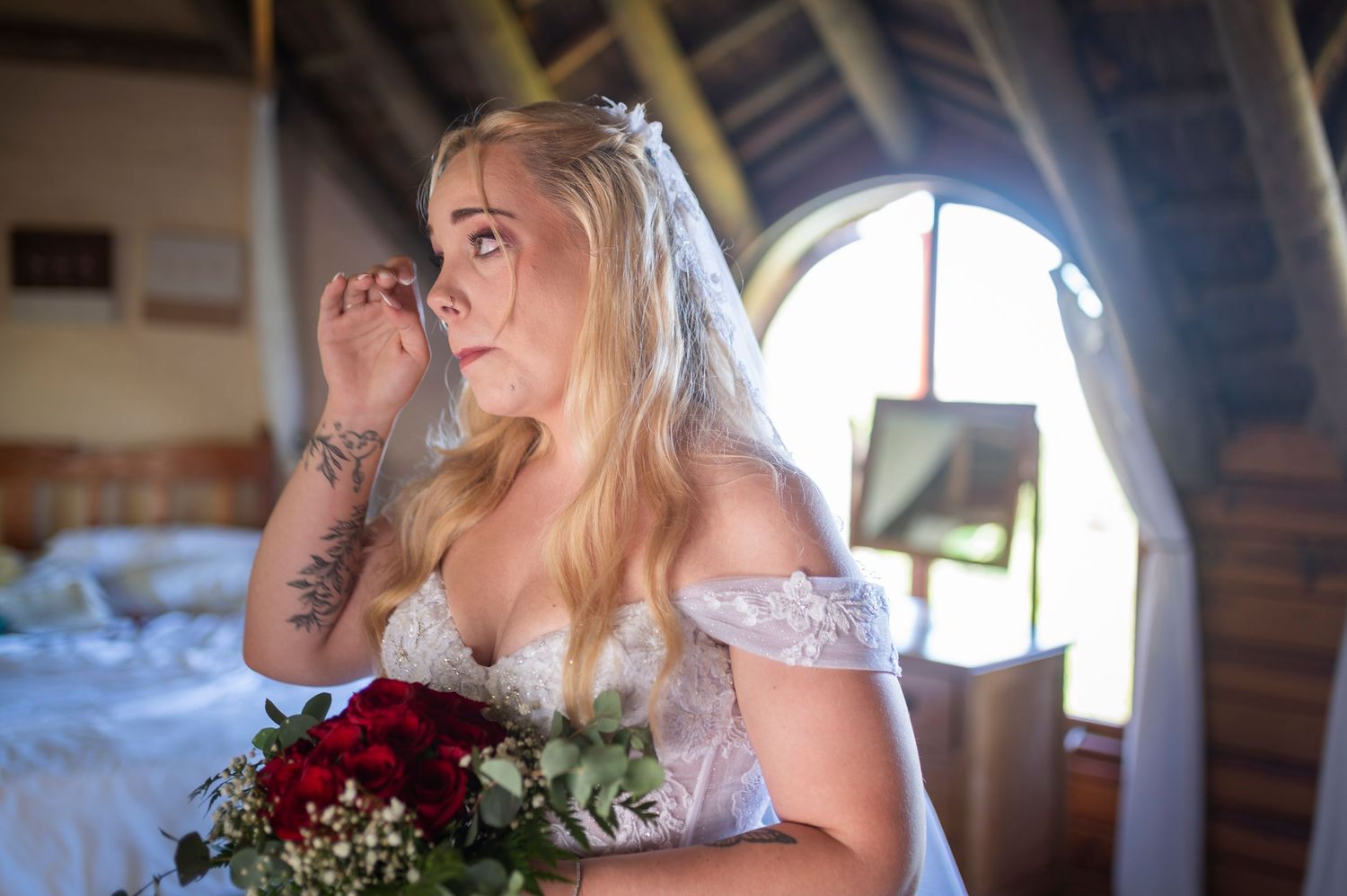 A person in turquoise helps adjust a delicate white wedding veil in a sunlit wooden cabin room.