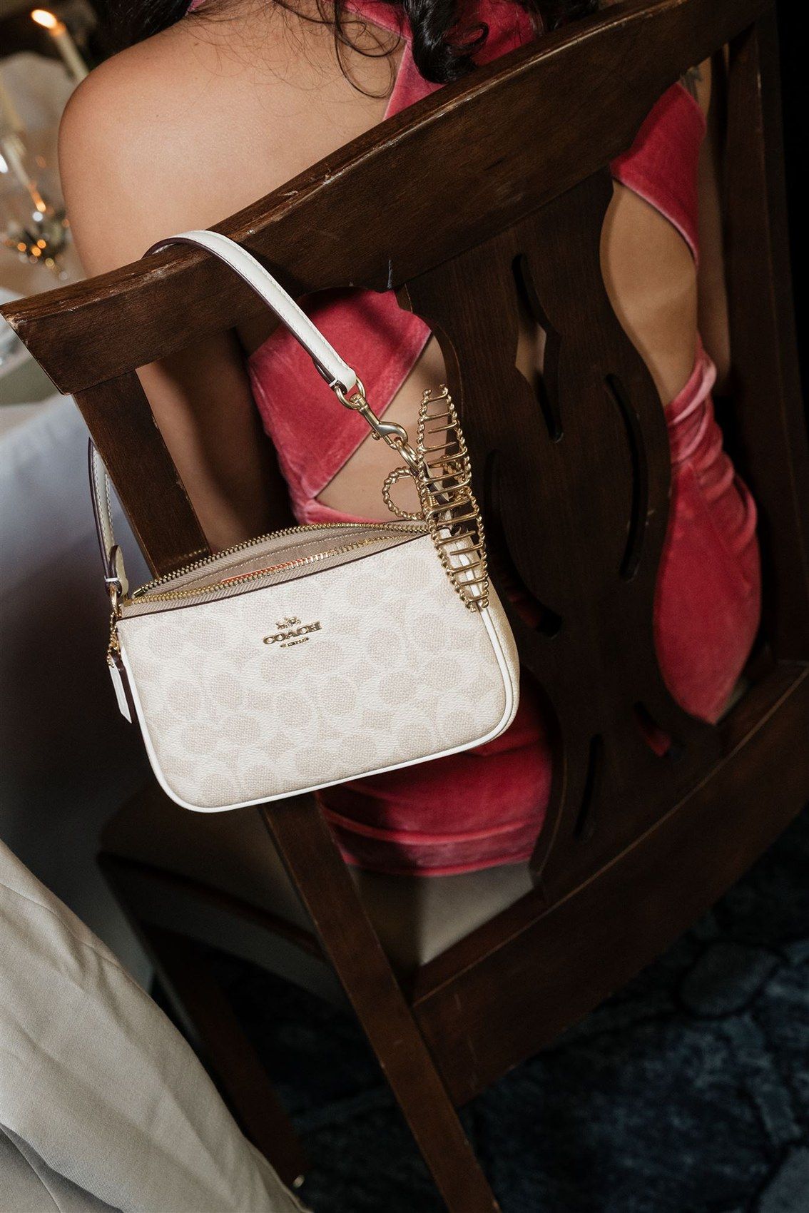 A white Coach handbag and red shoes displayed on dark wooden furniture.