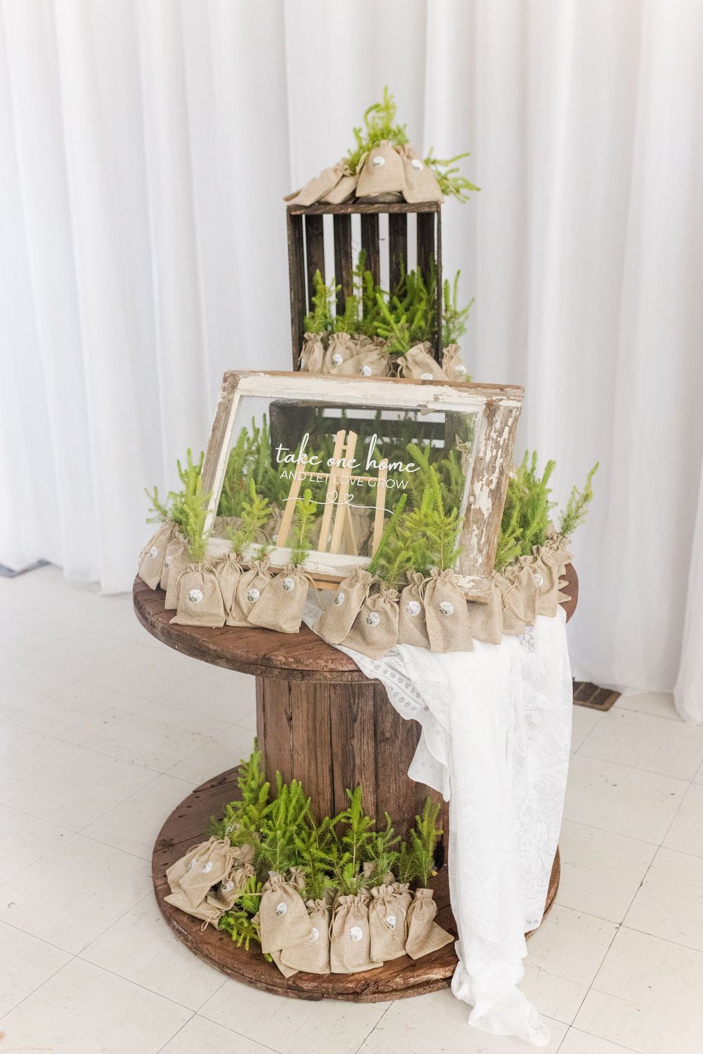 Rustic wooden spool table display with decorative birdcage, frame, and greenery arrangements for a wedding event.