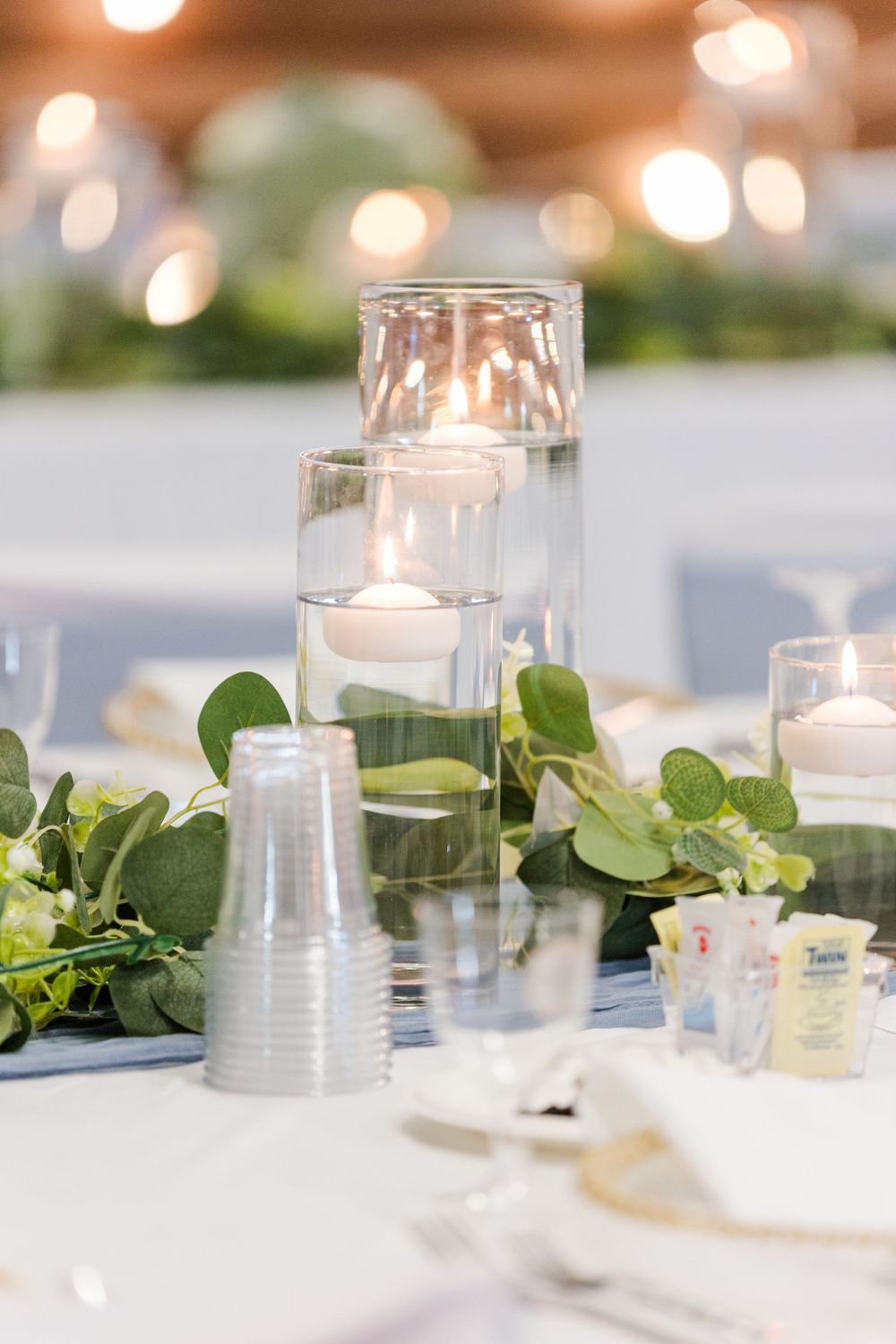White candles in glass votives with fresh eucalyptus leaves create an elegant tablescape decoration.