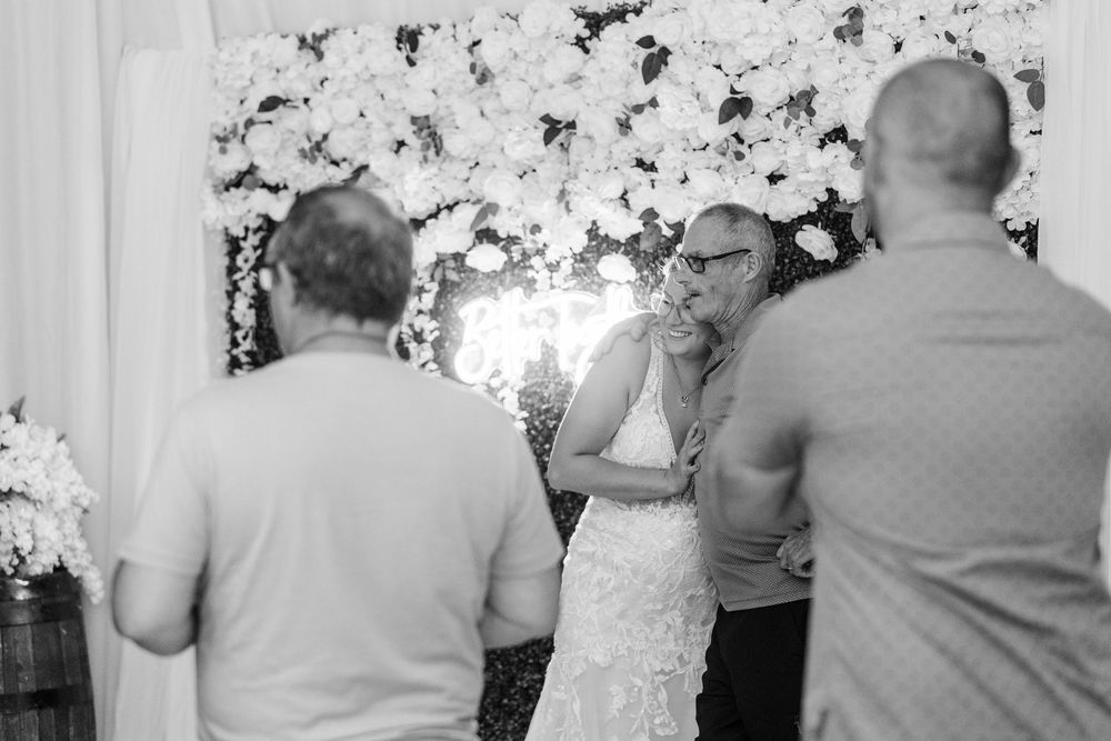 Black and white photo of a wedding ceremony in front of a floral backdrop with people gathered at the altar.