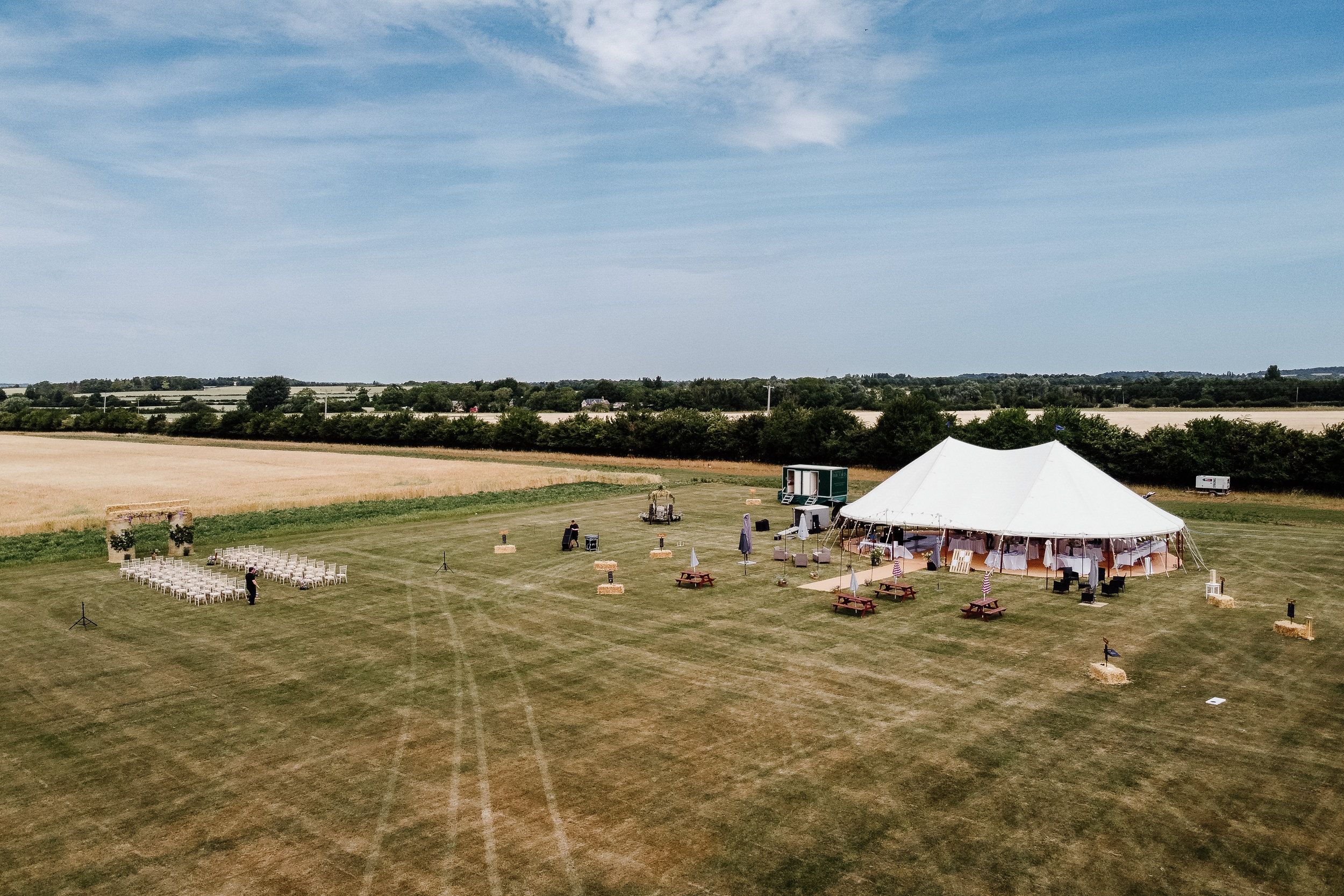 Aerial view of multiple outdoor sports fields with white tents and people gathering for an event on green grass.