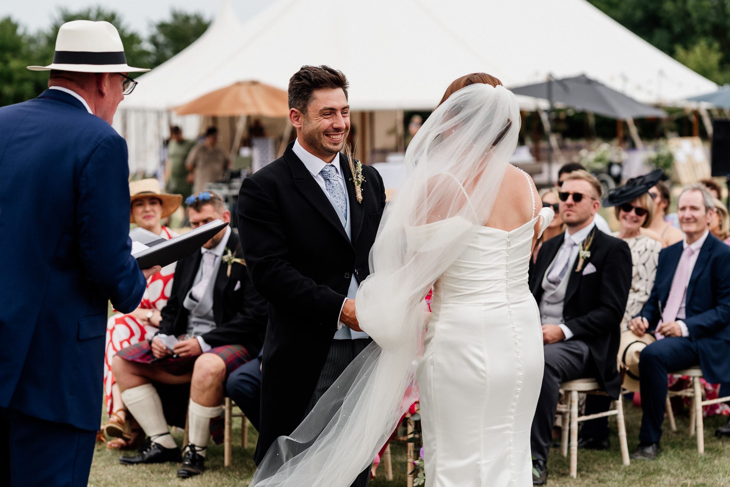 Elegant outdoor wedding ceremony setup with chairs arranged on grass and white tents in the background.