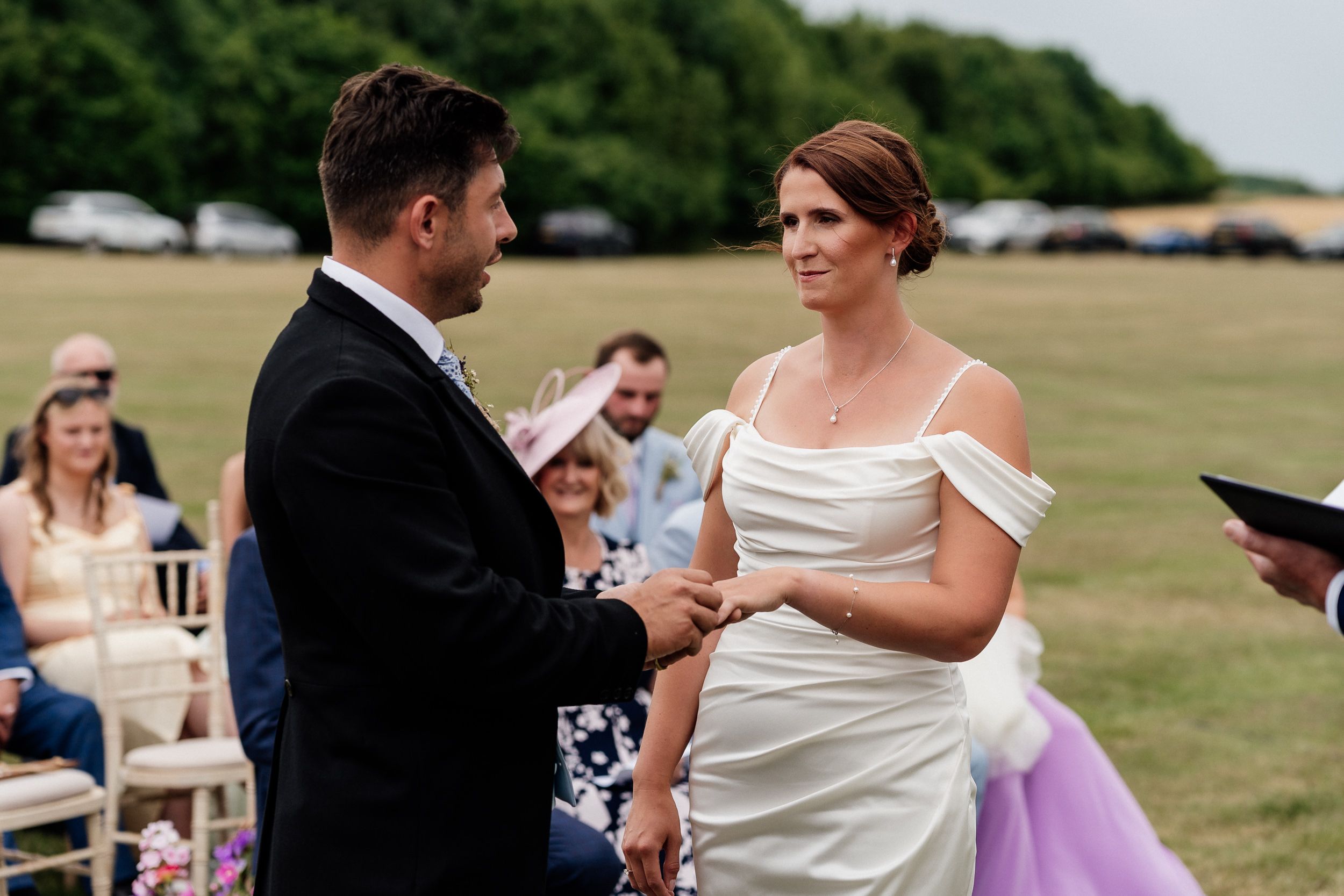 Wedding couple performing their first dance together outdoors with guests watching in the background at a sunny venue.