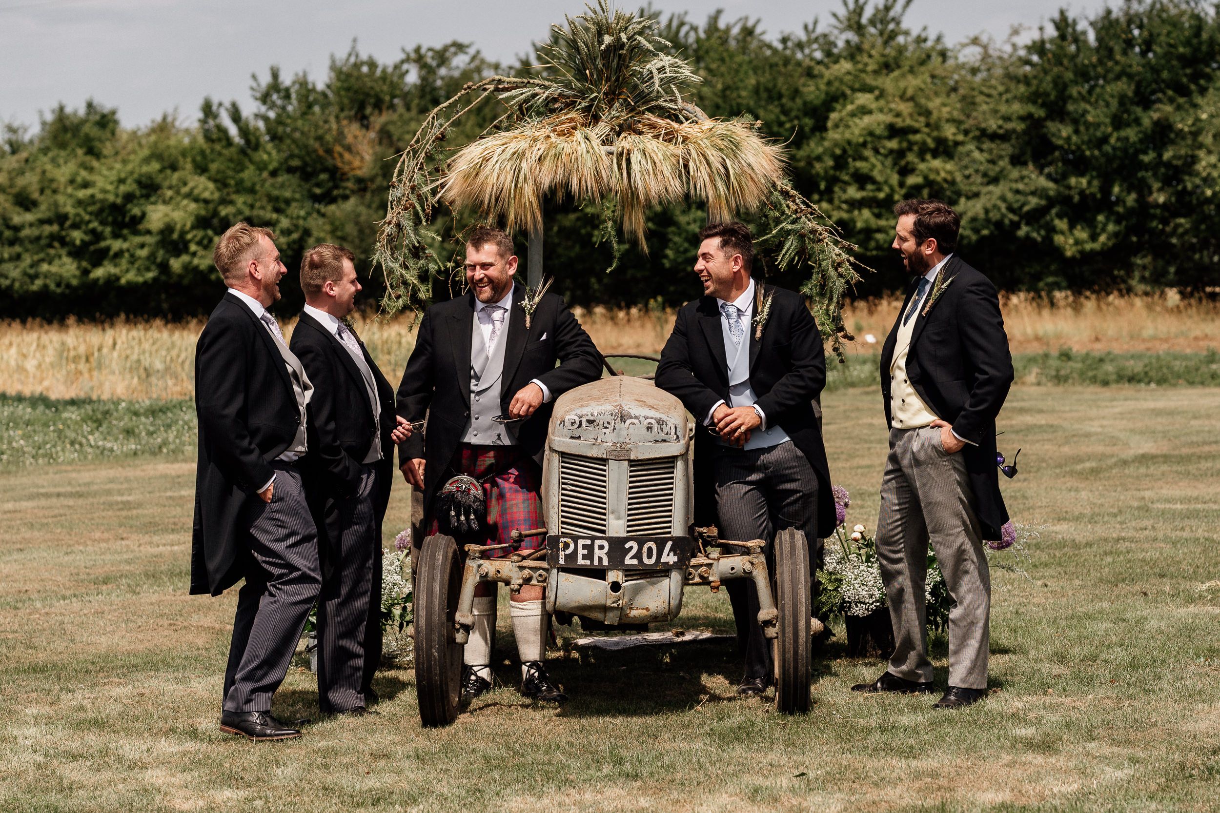 Group gathering outdoors at rustic wedding event with wooden benches arranged on grassy lawn during summer ceremony.