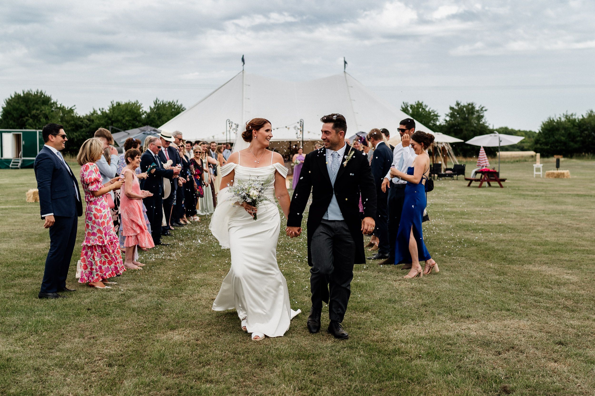 A wedding celebration on a grassy field with guests lined up outdoors under cloudy skies.