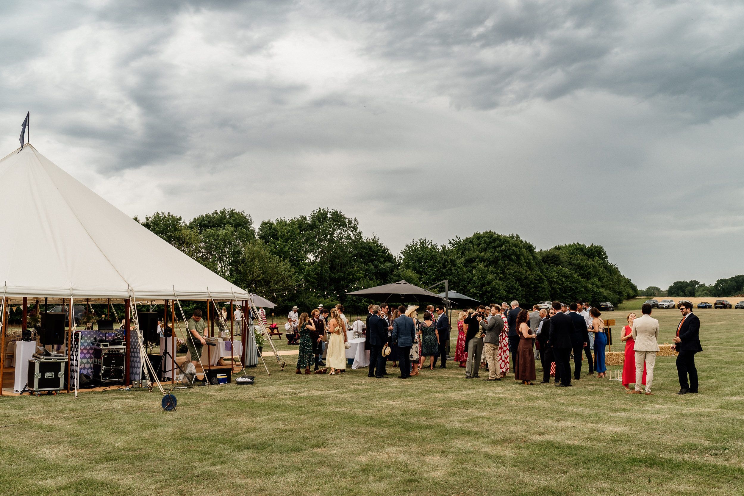 A panoramic view of a large outdoor farm wedding reception under white tents during an overcast day.