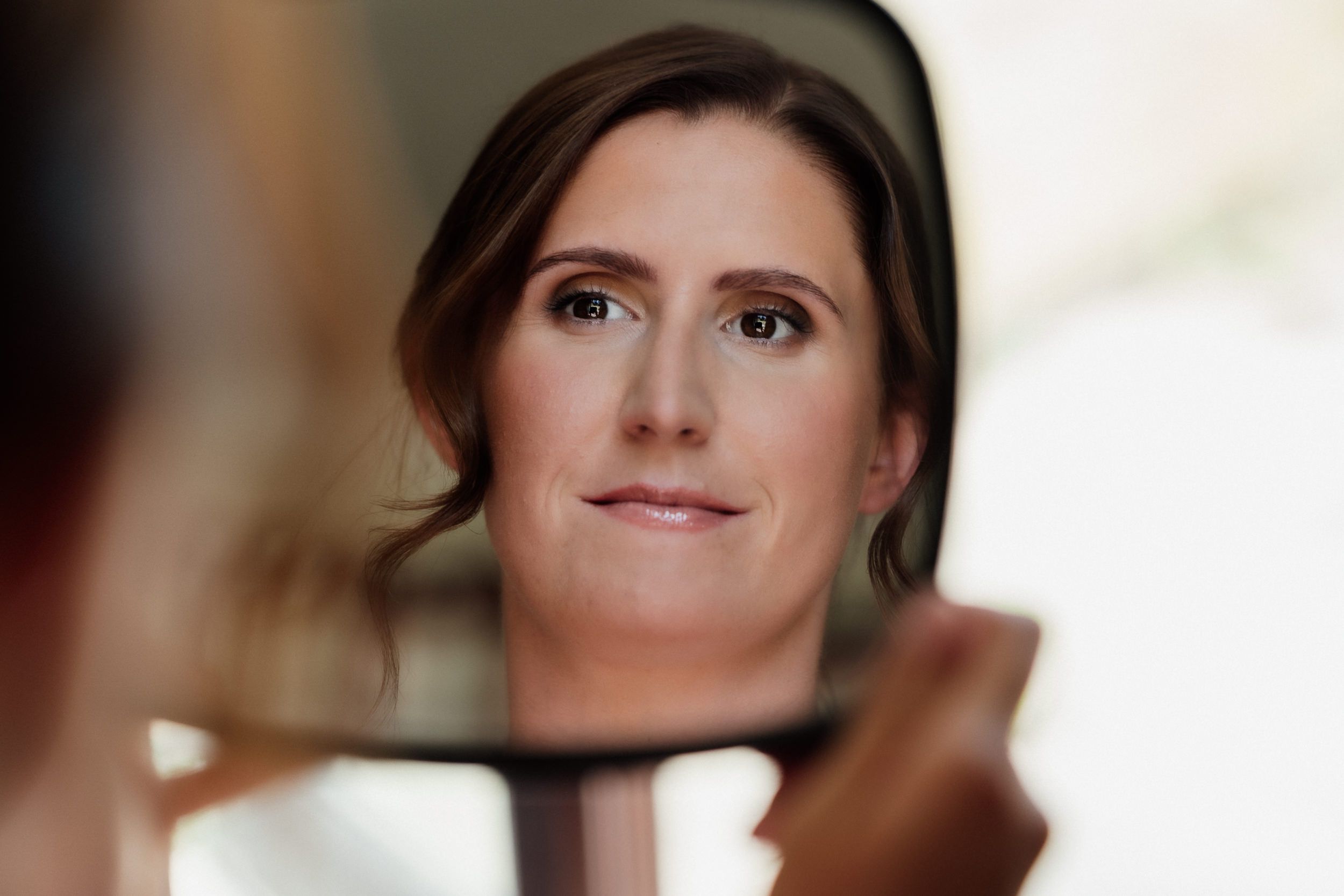 A reflection in a mirror shows a gentle smile and side-swept dark hair against a soft blurred background.
