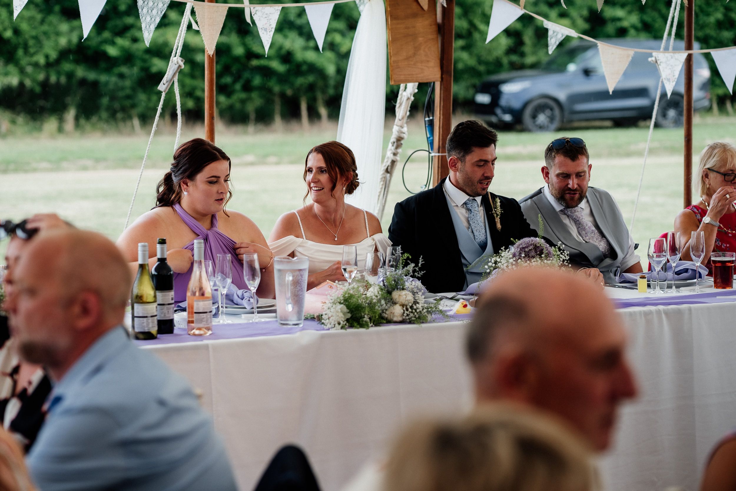 Guests seated at long tables during an outdoor wedding reception under white tents.