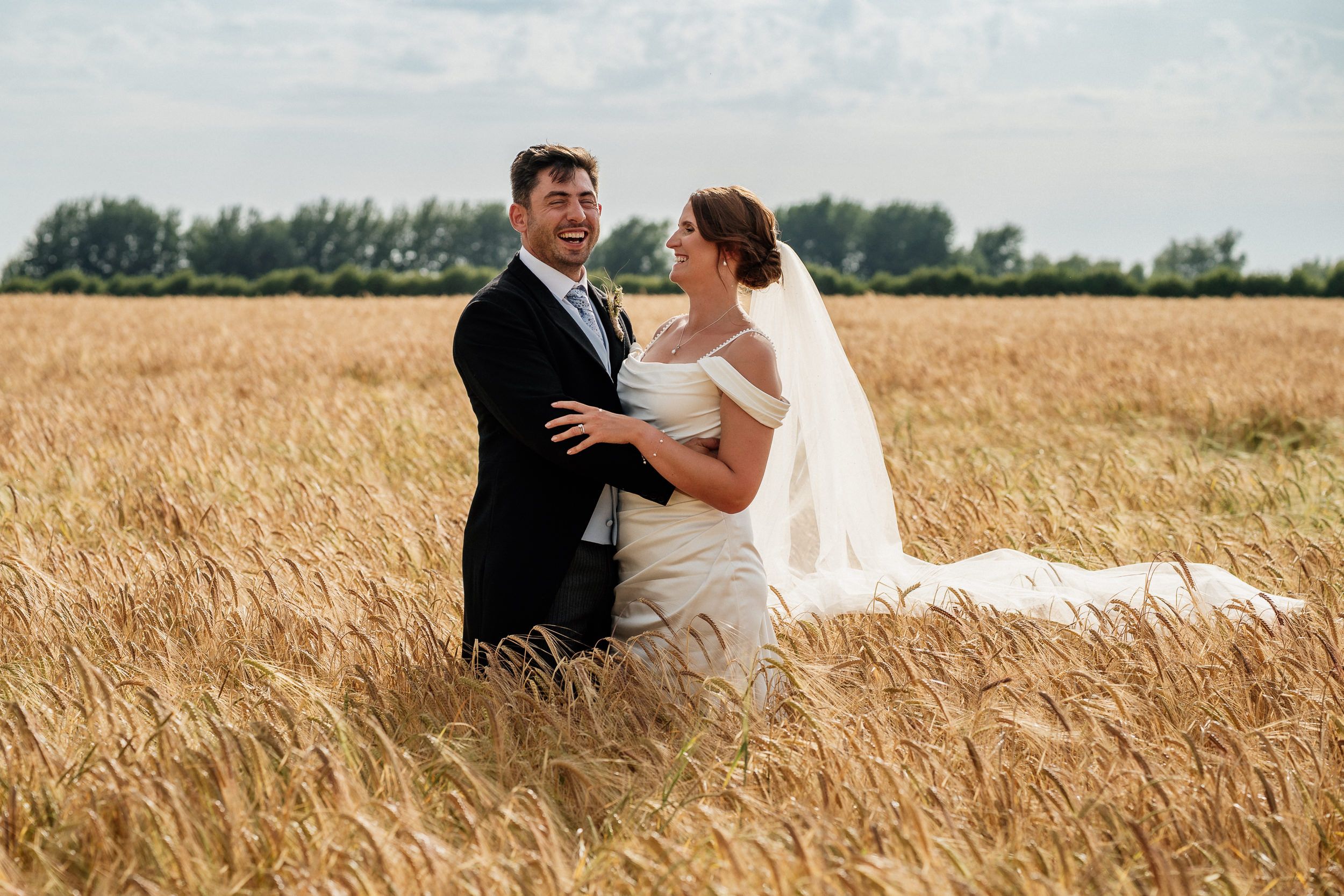 A romantic wedding couple embraces while standing in a golden wheat field during a sunny summer day.