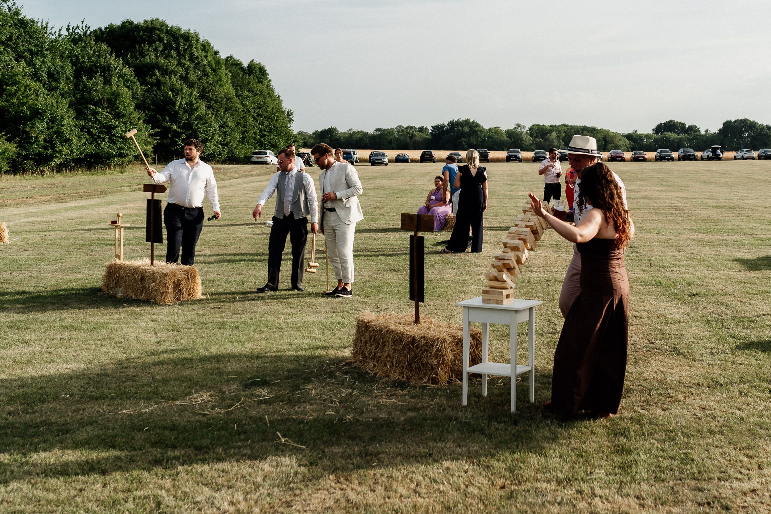 Outdoor lawn game setup at a rustic wedding reception in Cambridgeshire with hay bales and guests gathering around tables.