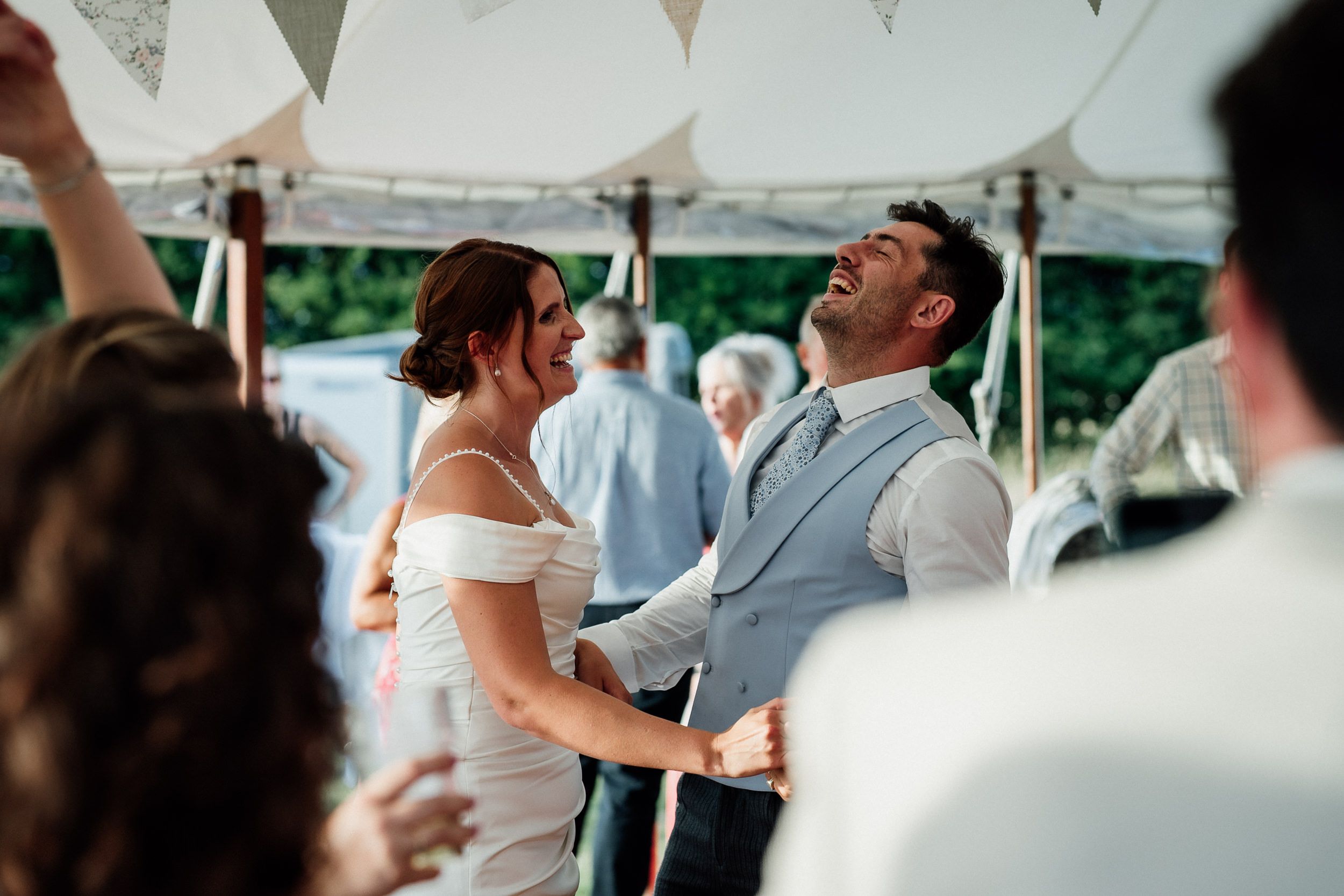 Happy couple sharing a joyful moment during their outdoor wedding celebration under a white tent.