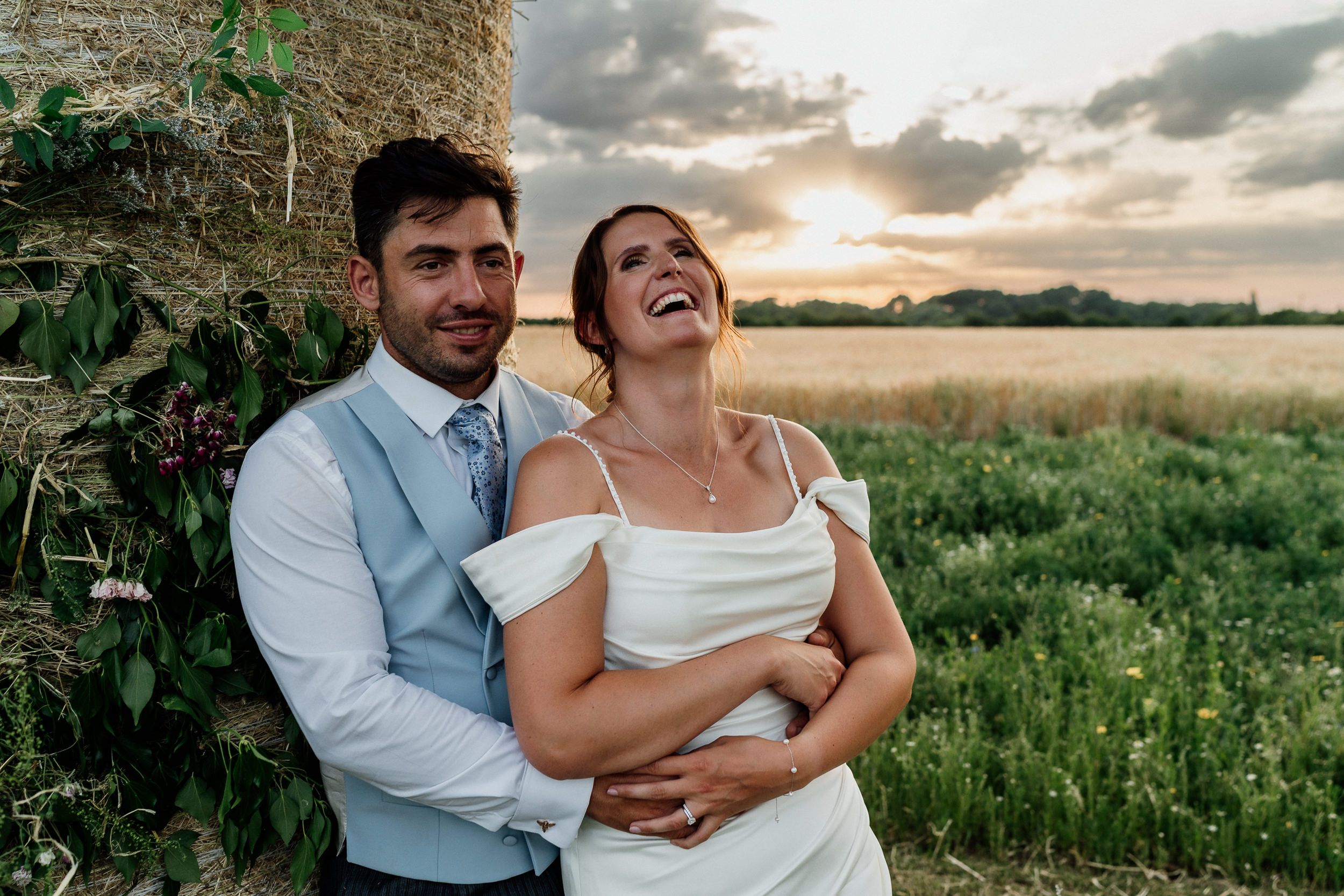A couple shares a joyful, candid moment together in a field during golden hour sunset - photo by Peter Oliver.