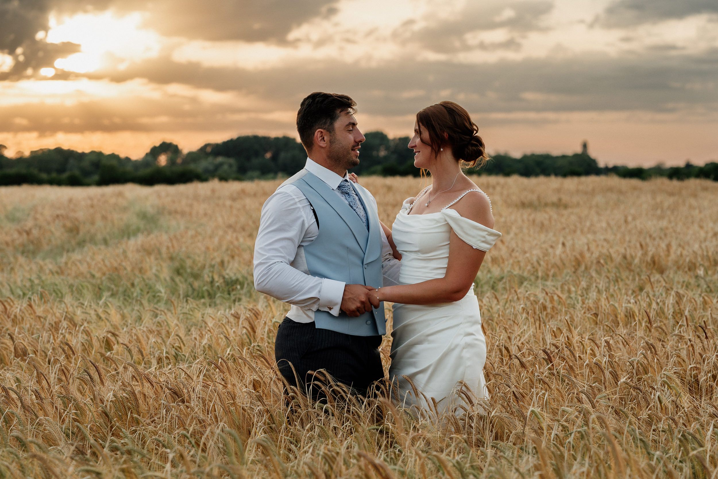 A romantic couple together in a field at sunset as dramatic clouds fill the sky above, taken by a Cambridge wedding photographer.