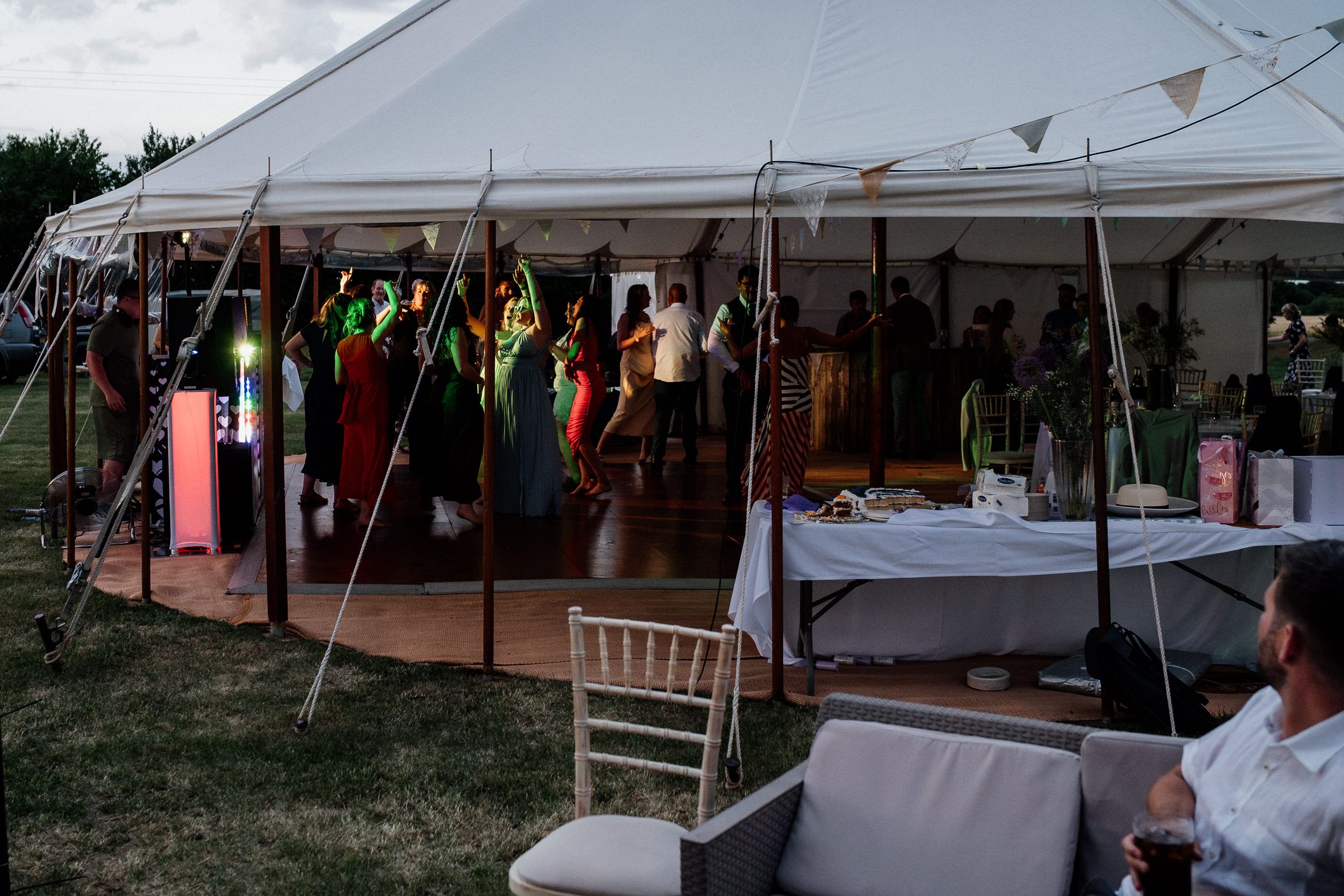 People gather under a white outdoor tent at dusk for a reception with tables and chairs set up on a lawn.