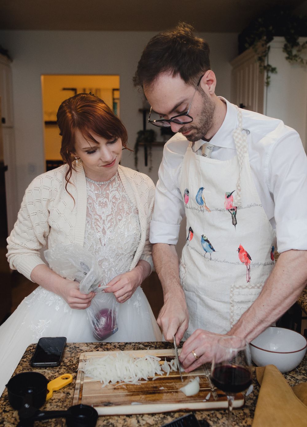 Two people in white attire prepare ingredients together at a wooden cutting board in a kitchen setting.