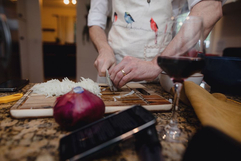 Professional chef hands chopping red onions on a wooden cutting board with a sharp knife in kitchen lighting.