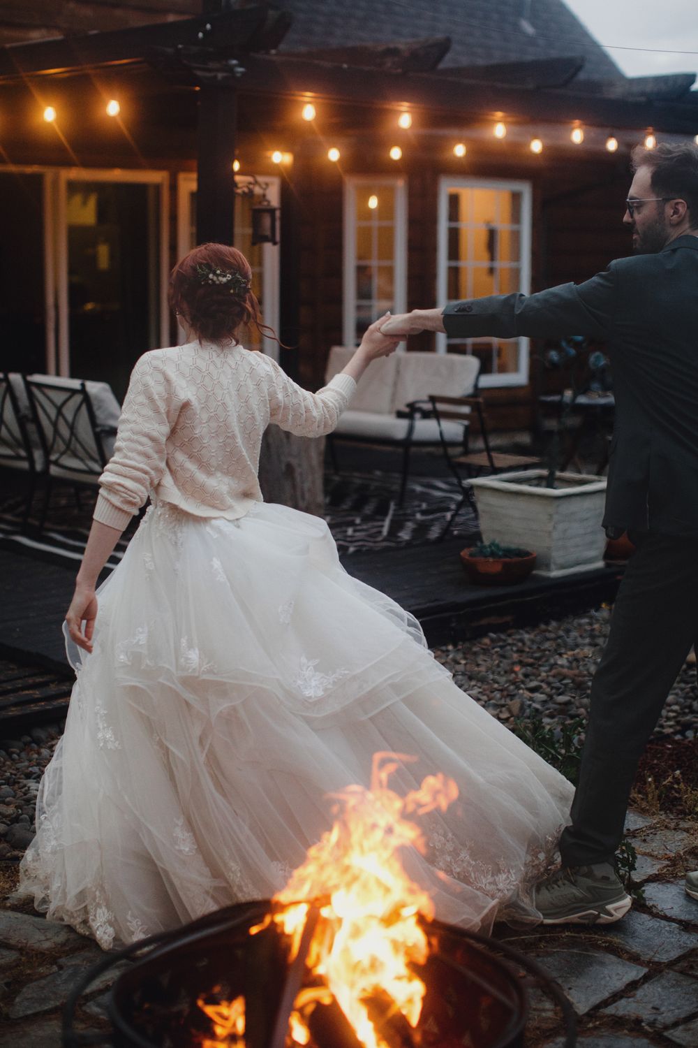 A couple dancing outdoors at night by a fire pit with string lights illuminating the patio of a rustic venue.