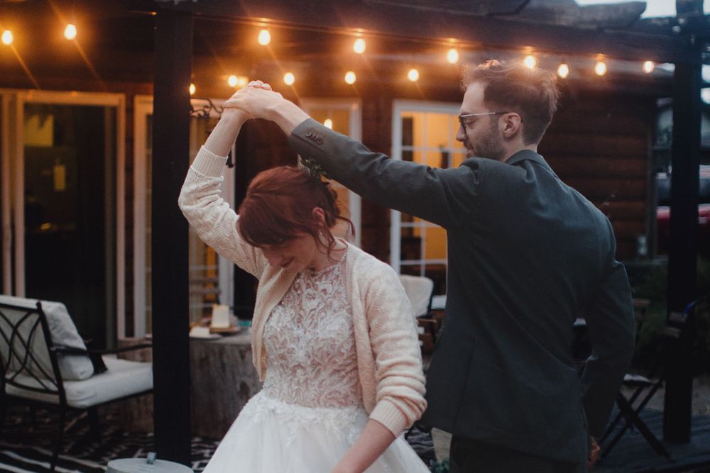 A couple shares a romantic dance under warm string lights on an outdoor patio during their wedding celebration.