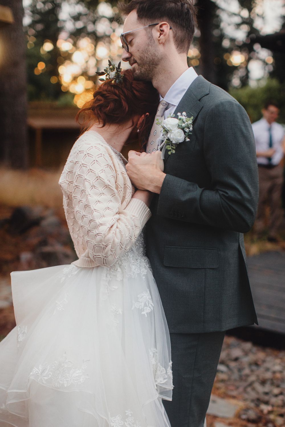 Romantic outdoor wedding moment at sunset with couple embracing in vintage-inspired lace gown and dark suit.