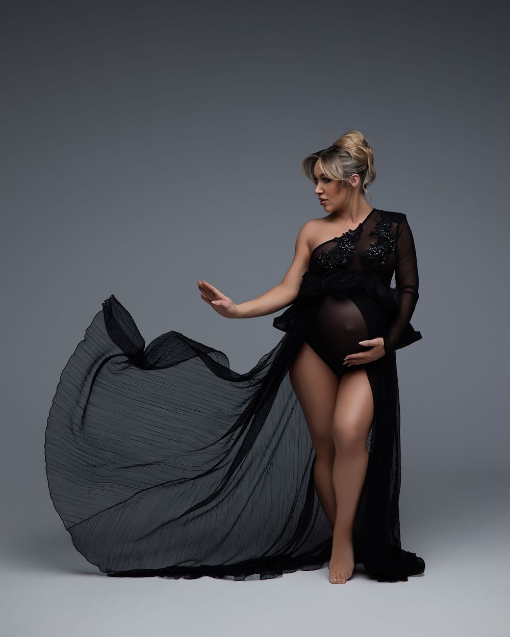 Graceful figure in black dress photographed in dramatic movement sequence against grey studio backdrop.