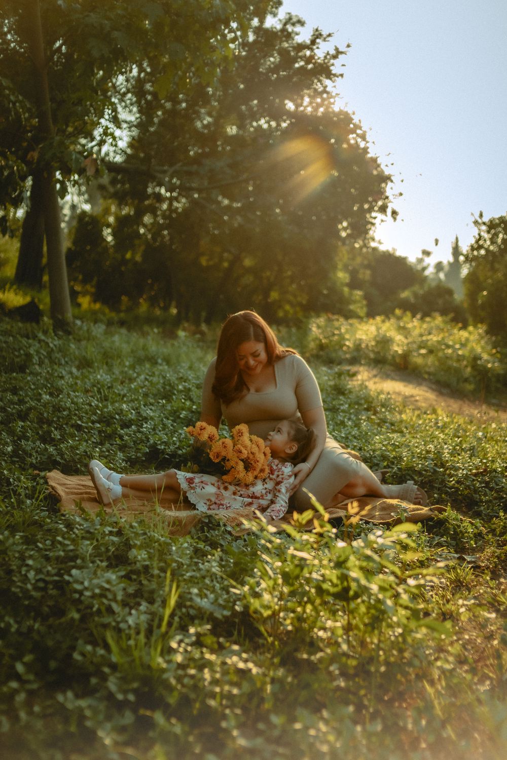 Mother and daughter sitting on a blanket in the park with the sunlight behind them
