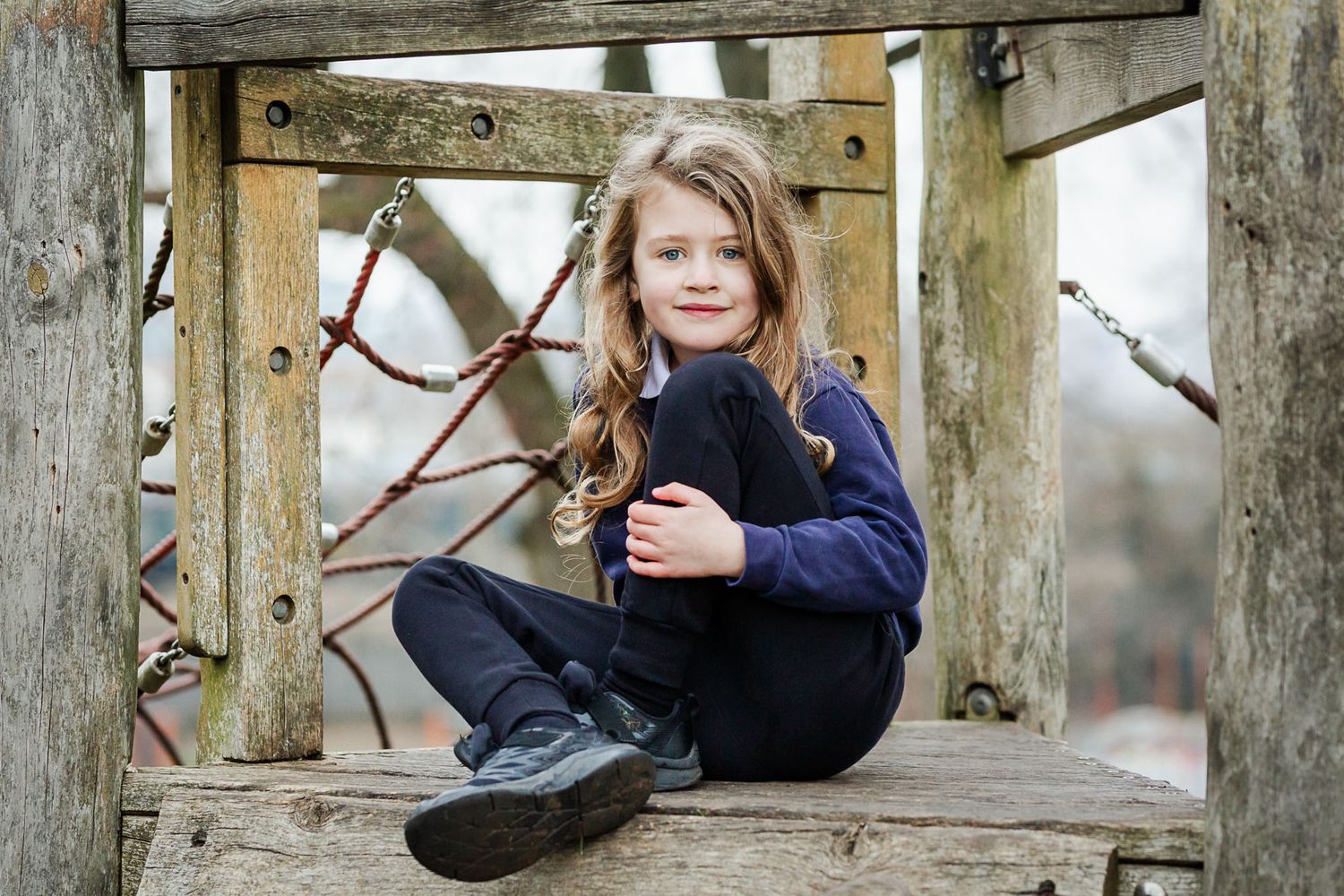 A primary school boy sits on a climbing frame and smiles naturally to the camera. He looks relaxed. Bristol nursery school photographer.
