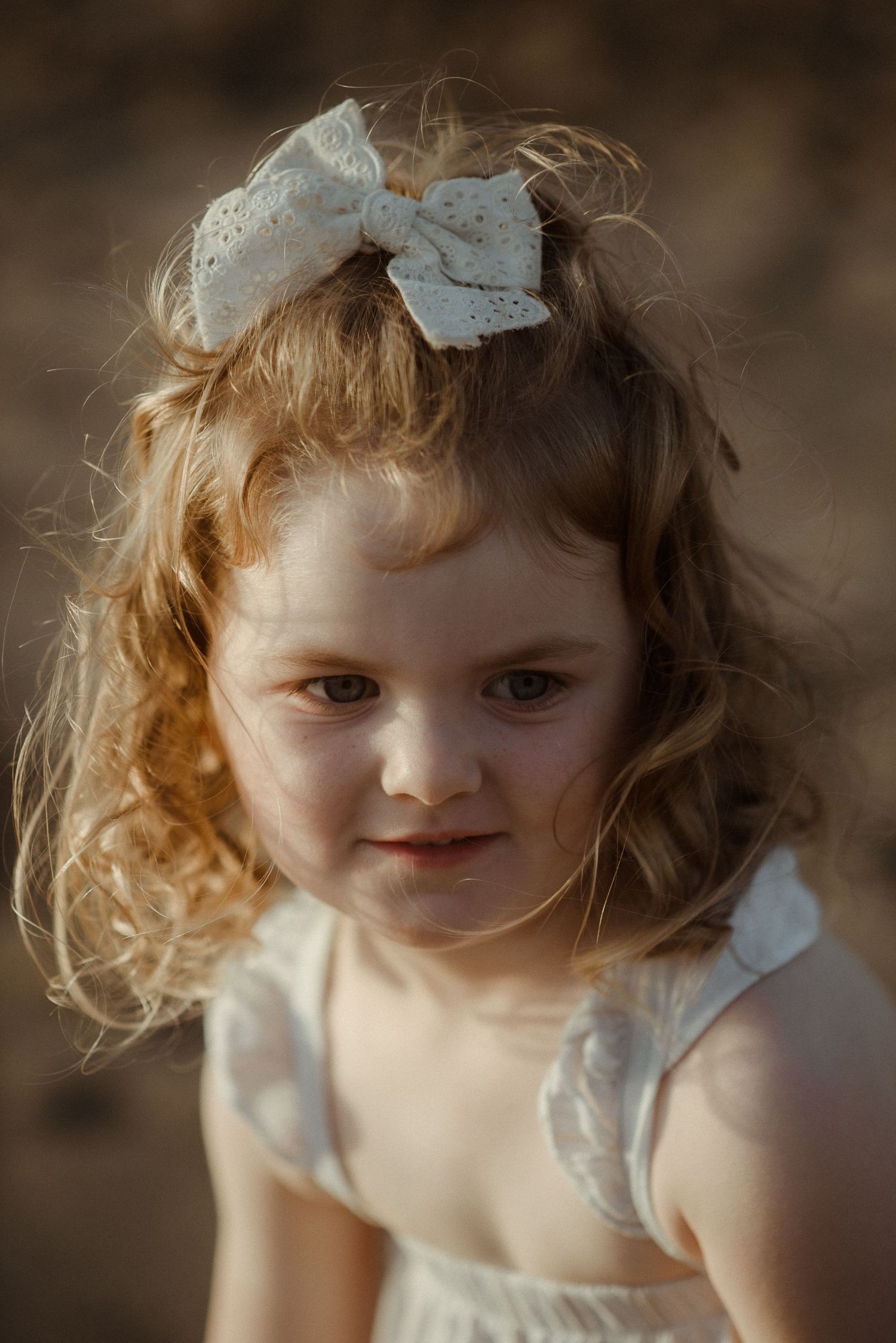 Portrait of child with curly hair wearing white dress and bow. Tenerife Wedding Photographer at Playa del Duque, Adeje.