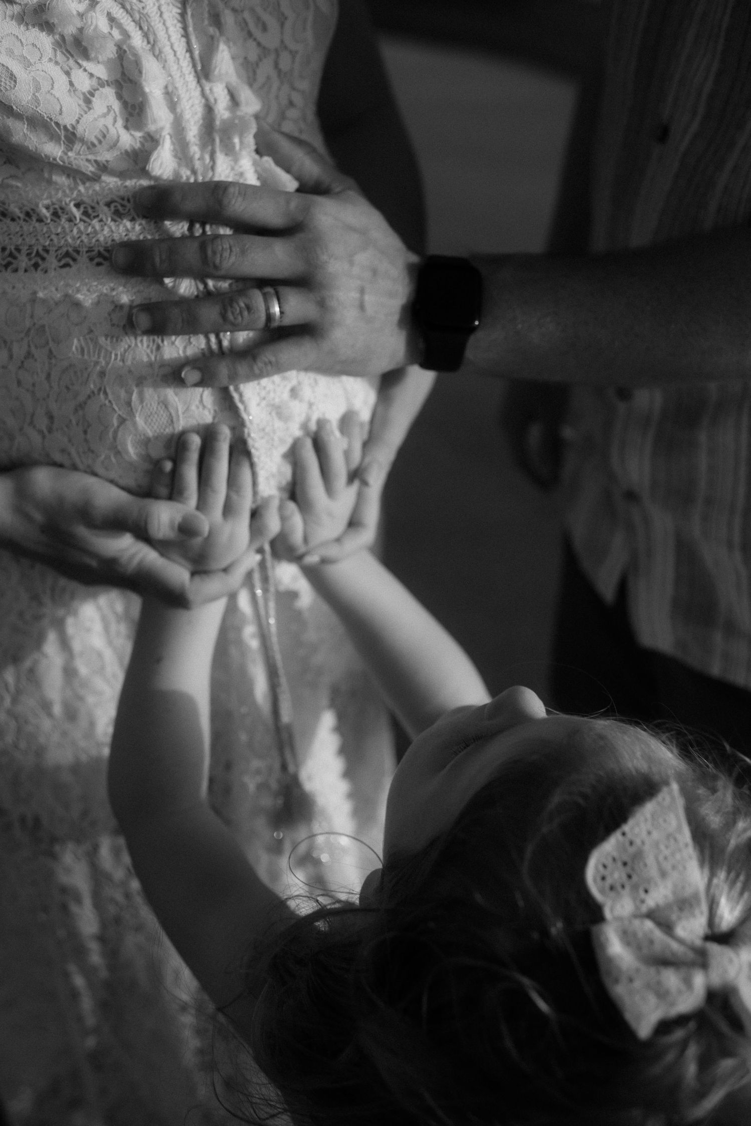 Black and white image of small hands reaching up to touch a white lace dress. Tenerife Wedding Photographer at Playa del Duque, Adeje.