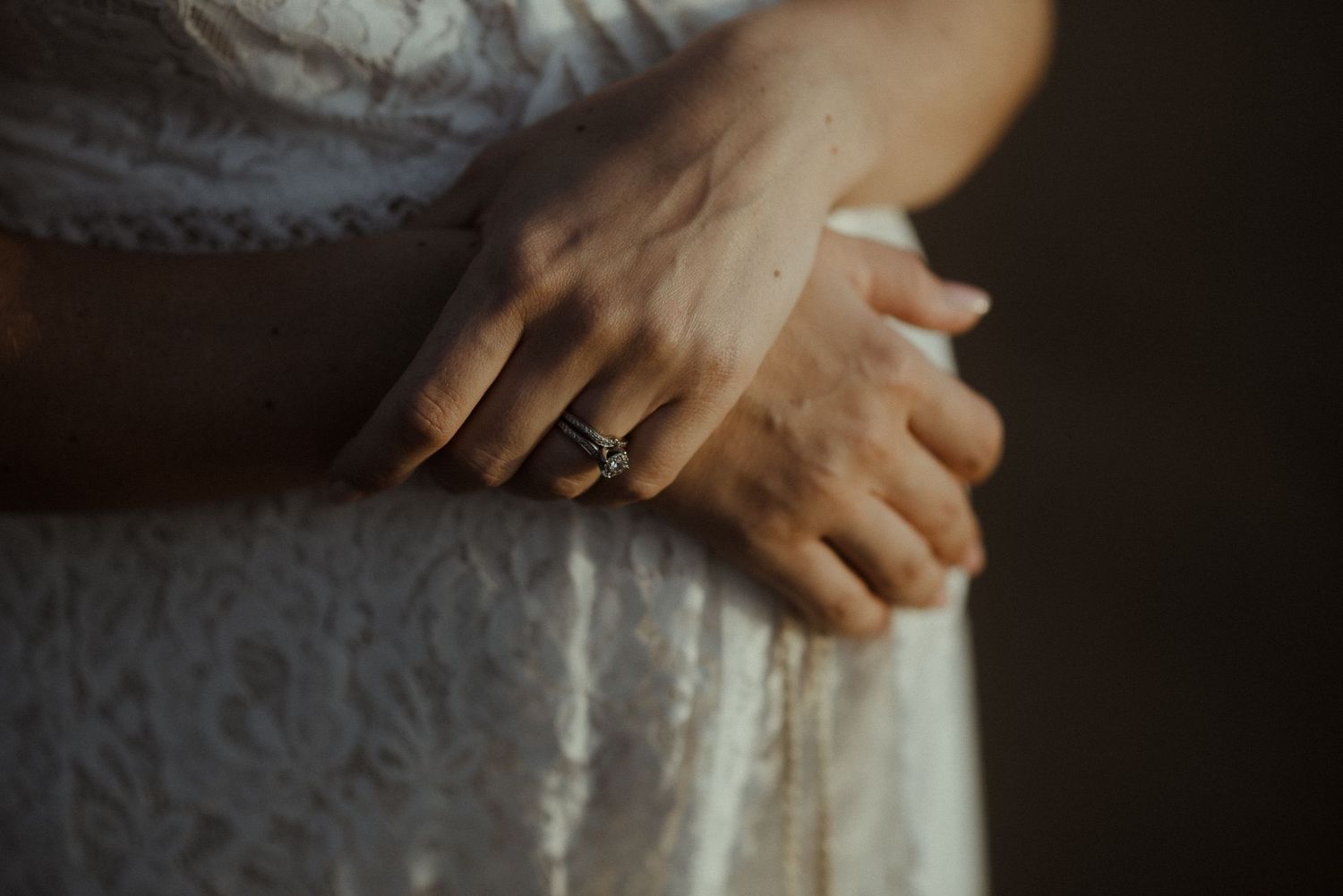 Close-up shot of hands with an engagement ring against a white lace dress in moody lighting. Tenerife Wedding Photographer.