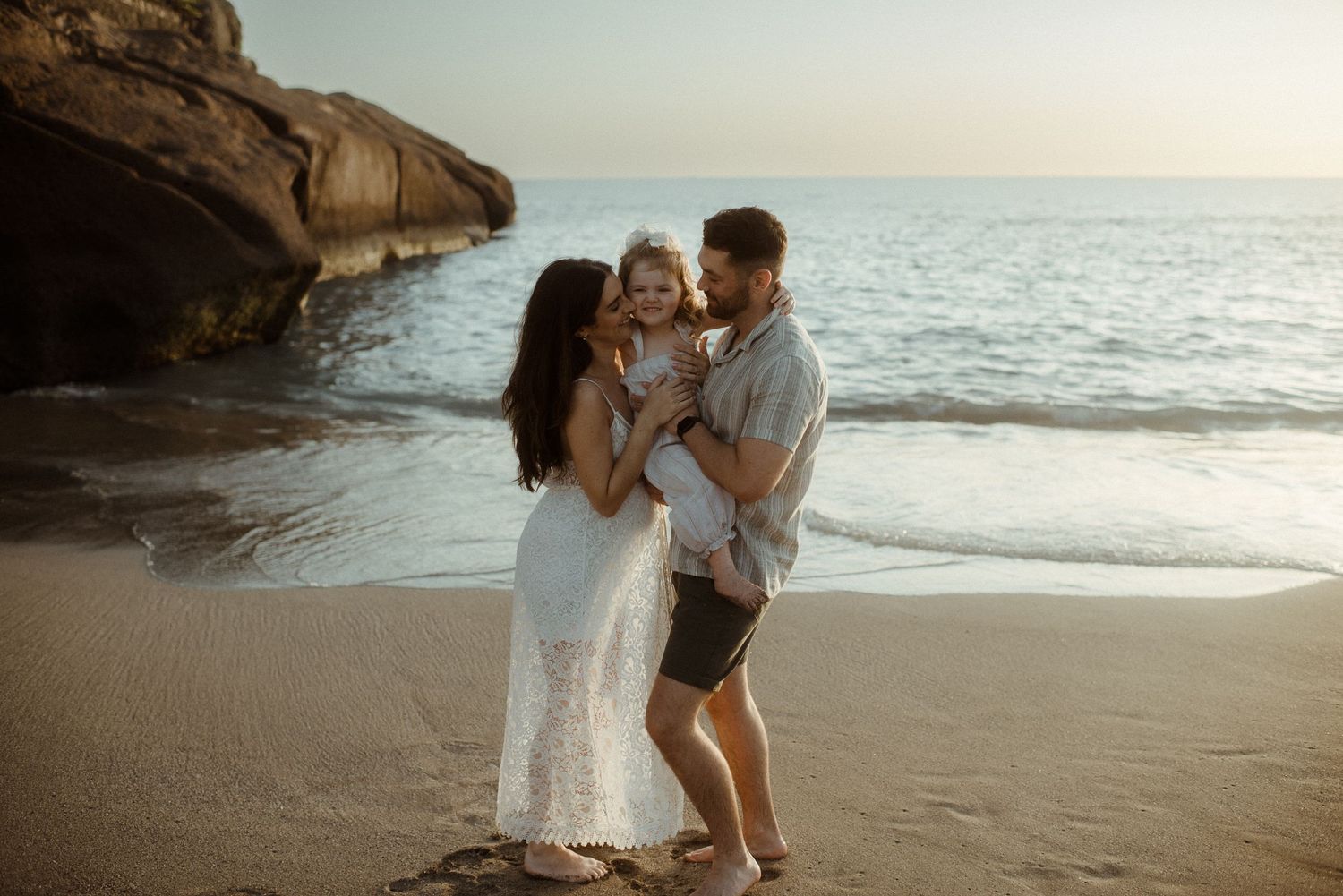 Family shares joyful moment together on beach at sunset near rocky cliffs. Tenerife Wedding Photographer at Playa del Duque, Adeje.