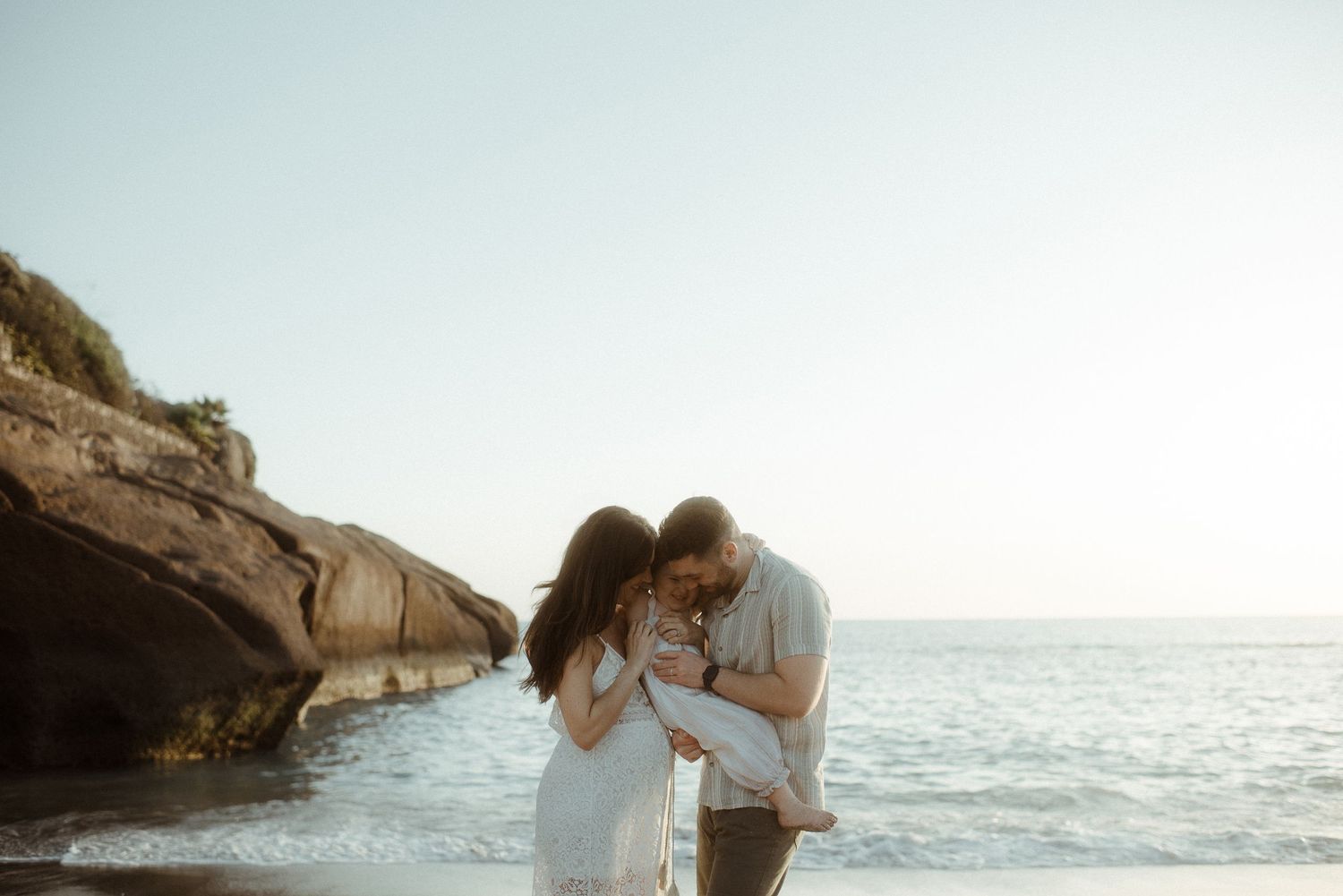 Intimate beachside moment between couple in white against rocky coastline. Tenerife Wedding Photographer at Playa del Duque, Adeje.