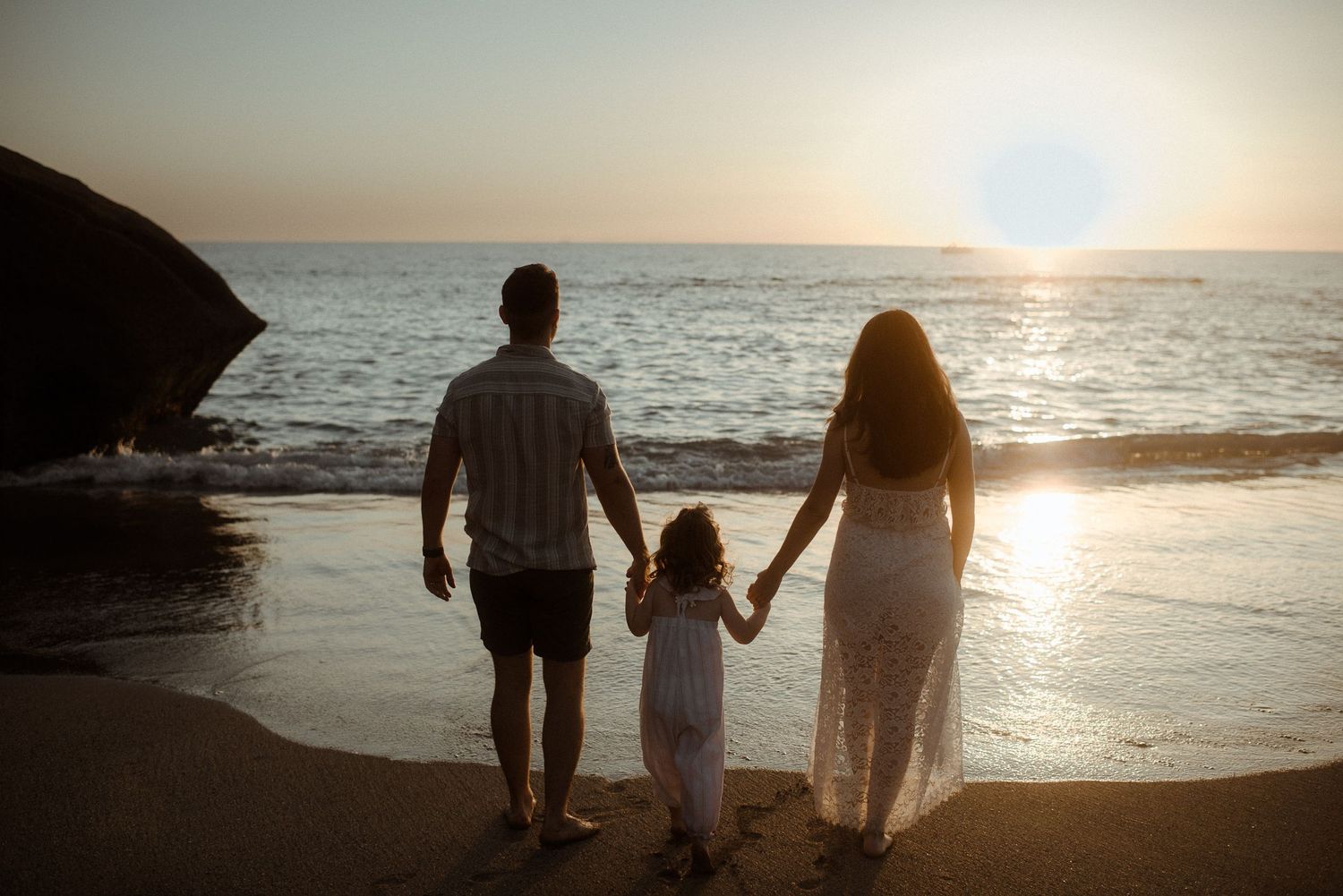 A family stands silhouetted against the setting sun on a beach. Tenerife Wedding Photographer at Playa del Duque, Adeje.